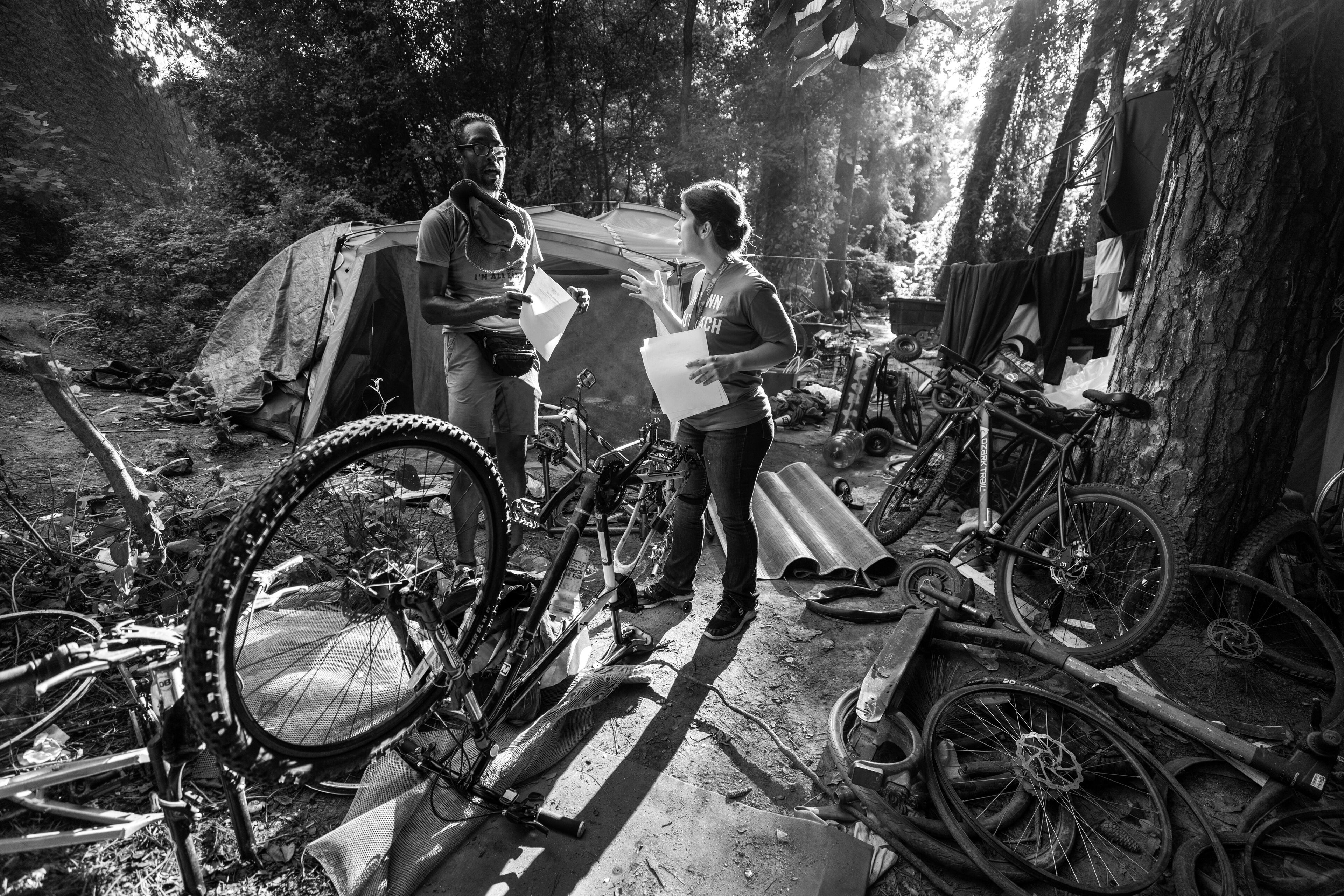 Intown Cares outreach representative Tracy Woodard talks with Ladell Hassell about an upcoming free medical care opportunity at a homeless encampment Along the banks of the North Fork of Peachtree Creek near Buford Highway, Tuesday, August 22, 2023. (Steve Schaefer/steve.schaefer@ajc.com)