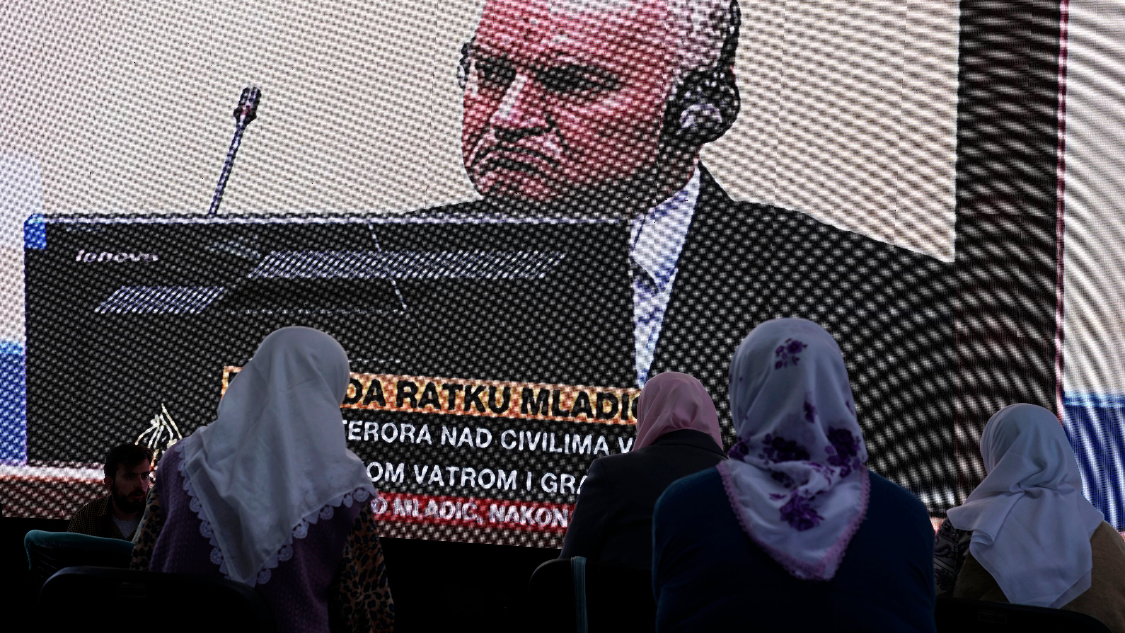 FILE - Women from Srebrenica watch a live broadcast from the Yugoslav War Crimes Tribunal in The Hague to learn the verdict for Bosnian Serb military chief Ratko Mladic, on the screen, at the memorial cemetery in Potocari near Srebrenica, eastern Bosnia, Tuesday, June 8, 2021.(AP Photo/Darko Bandic, File)