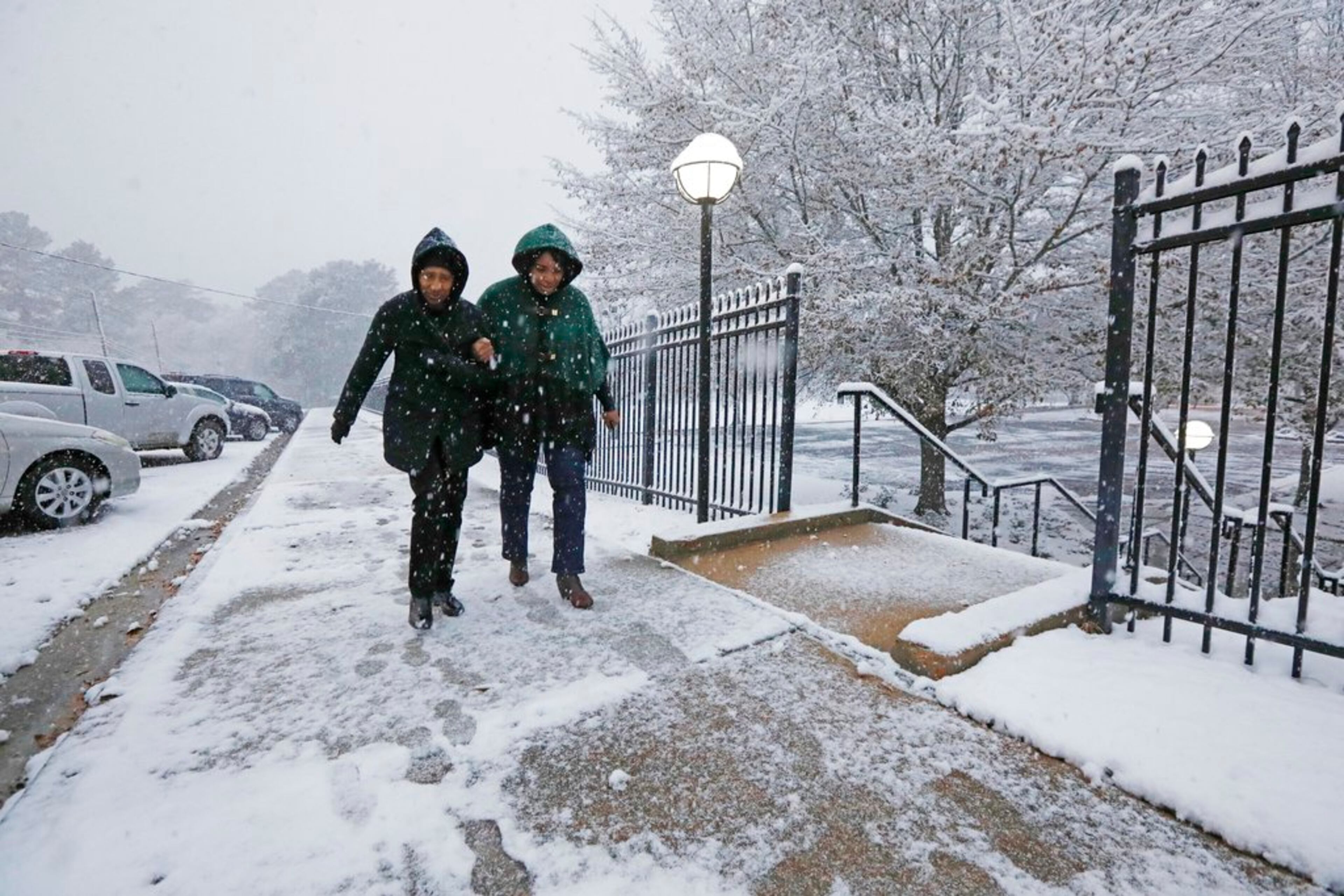 Worshippers link arms to avoid slipping as they walk along a snow-covered walkway to St. Richard Catholic Church to attend morning services, Friday, Dec. 8, 2017, in Jackson, Miss. The forecast called for a wintry mix of precipitation across several Deep South states. (AP Photo/Rogelio V. Solis)