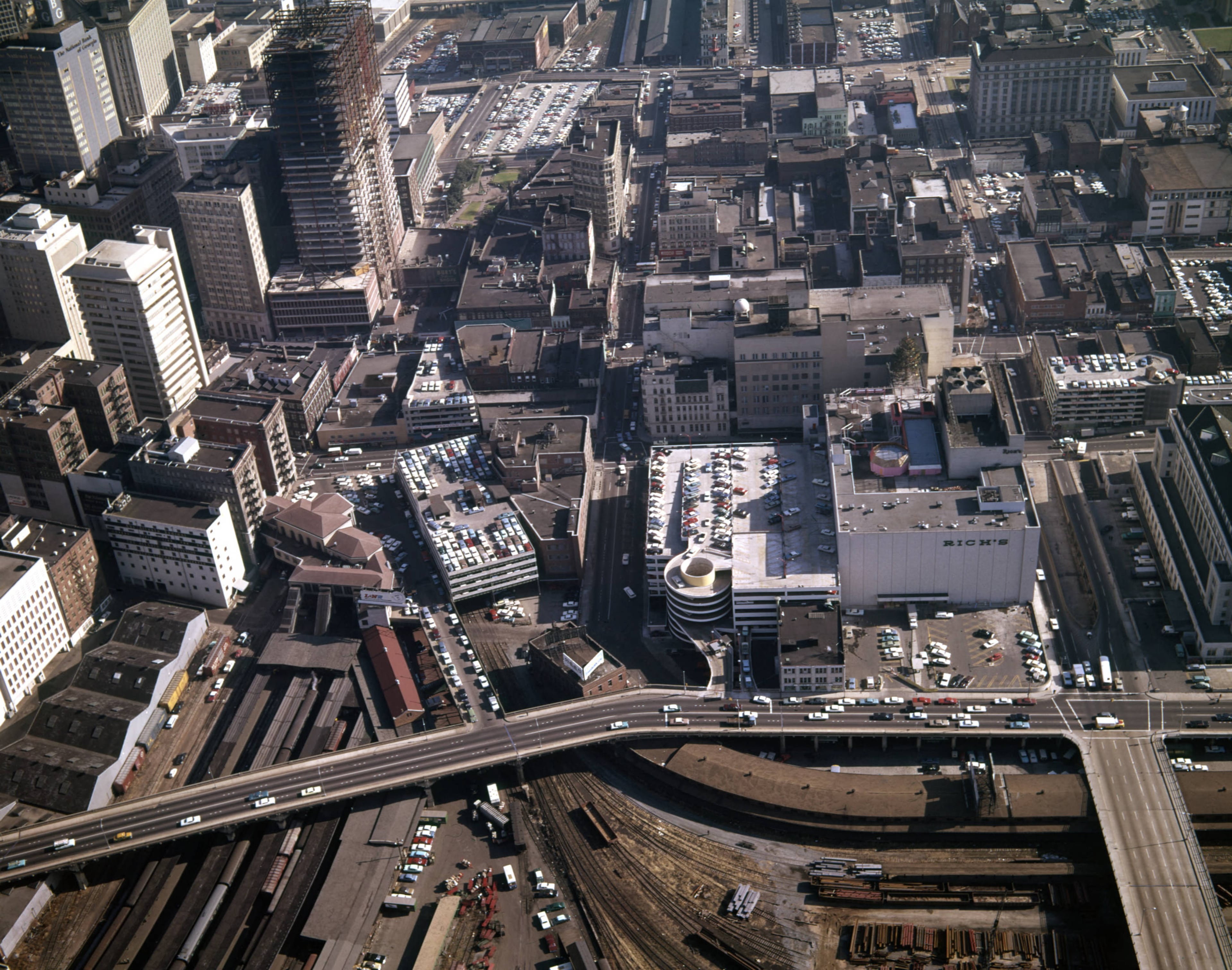 Aerial view of the city, looking east, showing the many parking lots and decks; the State of Georgia building is under construction, Atlanta, Georgia, December 21, 1965. Spring Street runs horizontally along the bottom.