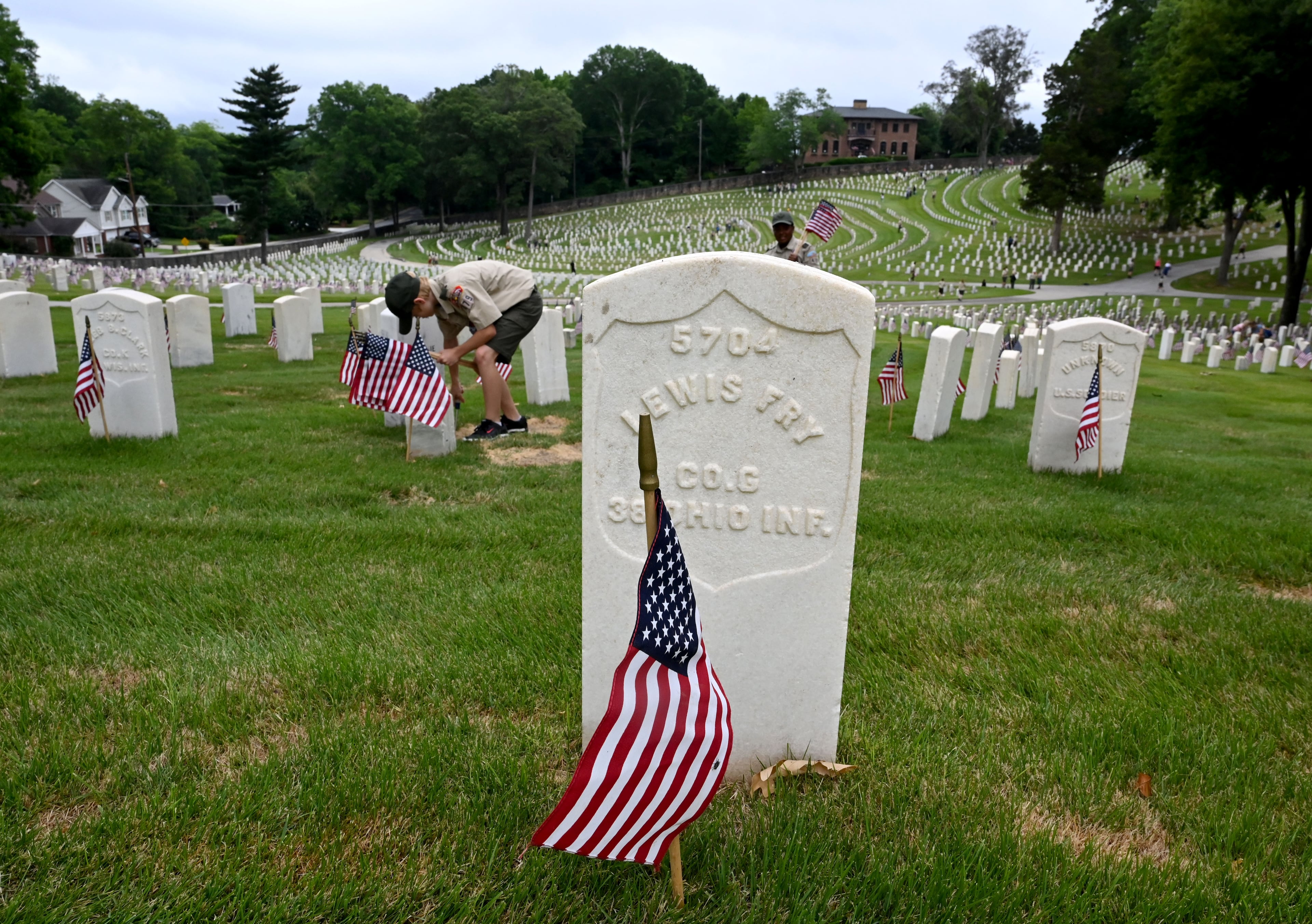Flags are placed in front of tombstones during the Memorial Day Flag Placement event at Marietta National Cemetery on Saturday, May 23, 2026, in Marietta. Scouting groups in the community place more than 18,000 U.S. veteran grave flags at Marietta National Cemetery each year on the Saturday before Memorial Day, helping prepare for Monday’s ceremony. The long-running service project—organized with the National Memorial Day Association of Georgia—also gives youth and adults an opportunity to honor fallen service members and learn about their sacrifices and the area’s history. (Hyosub Shin/AJC)