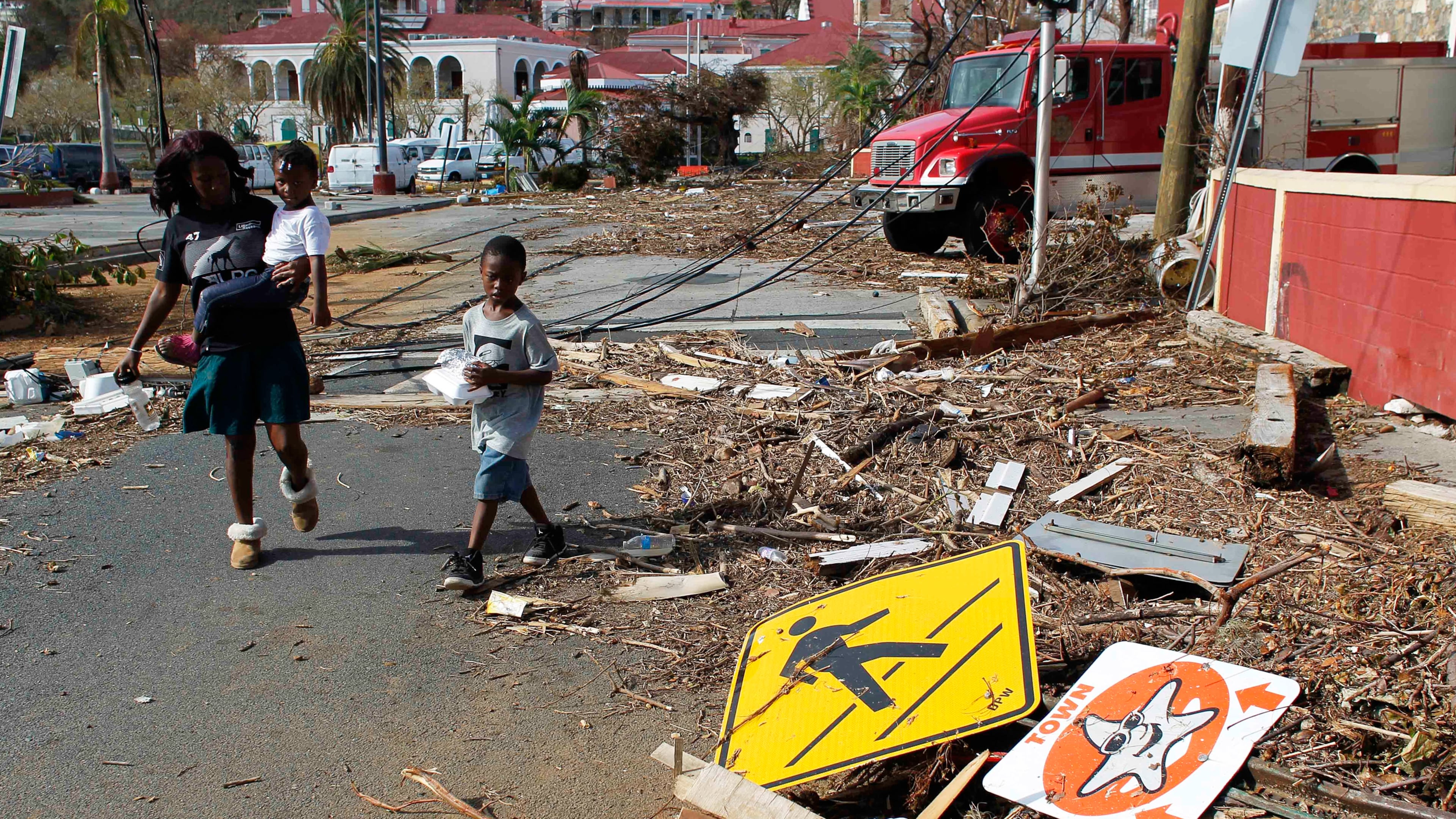 FILE - A woman and her children walk past debris left by Hurricane Irma in Charlotte Amalie, St. Thomas, U.S. Virgin Islands, on Sept. 10, 2017. (AP Photo/Ricardo Arduengo, File)