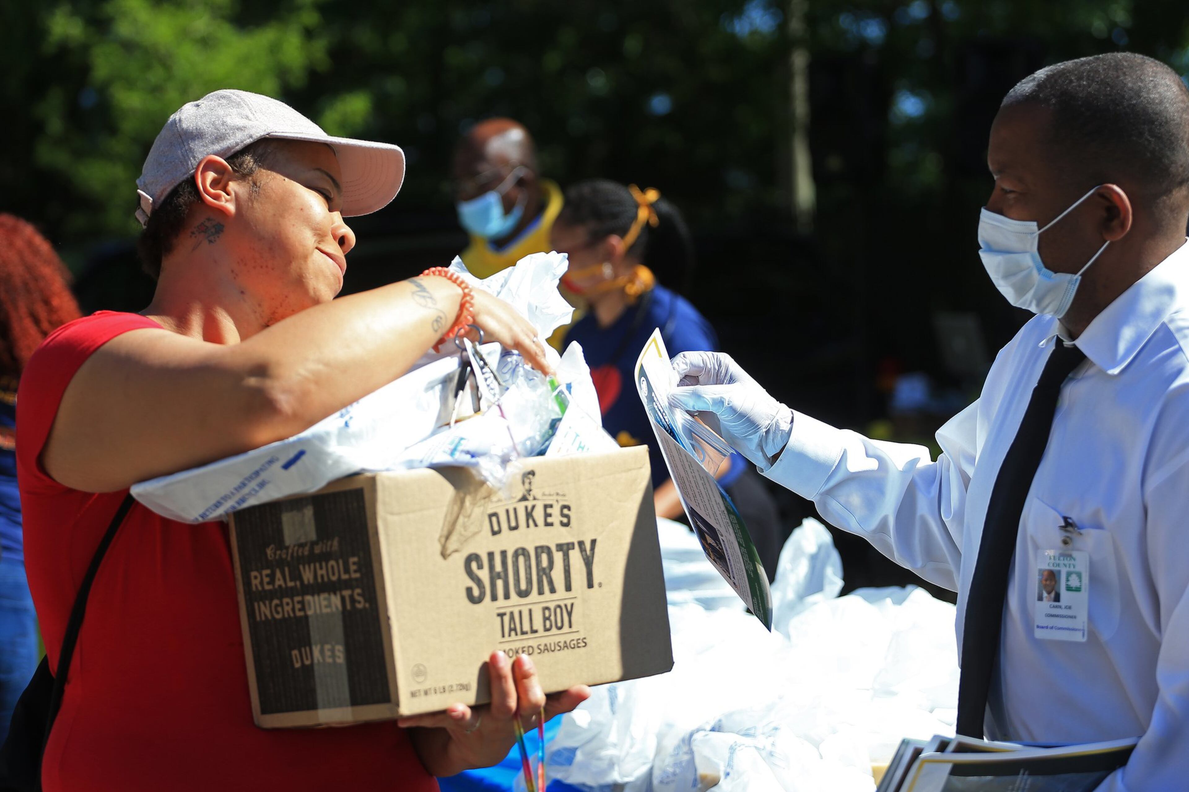 Joe Carn (right), Fulton County District 6 commissioner, hands a booklet to Danyell Vaughn during the Grab and Go free food and groceries event on Friday, April 17, 2020, at Allen Hills Apartments in Atlanta, which was organized to feed families during the coronavirus pandemic. (Christina Matacotta, for The Atlanta Journal-Constitution)