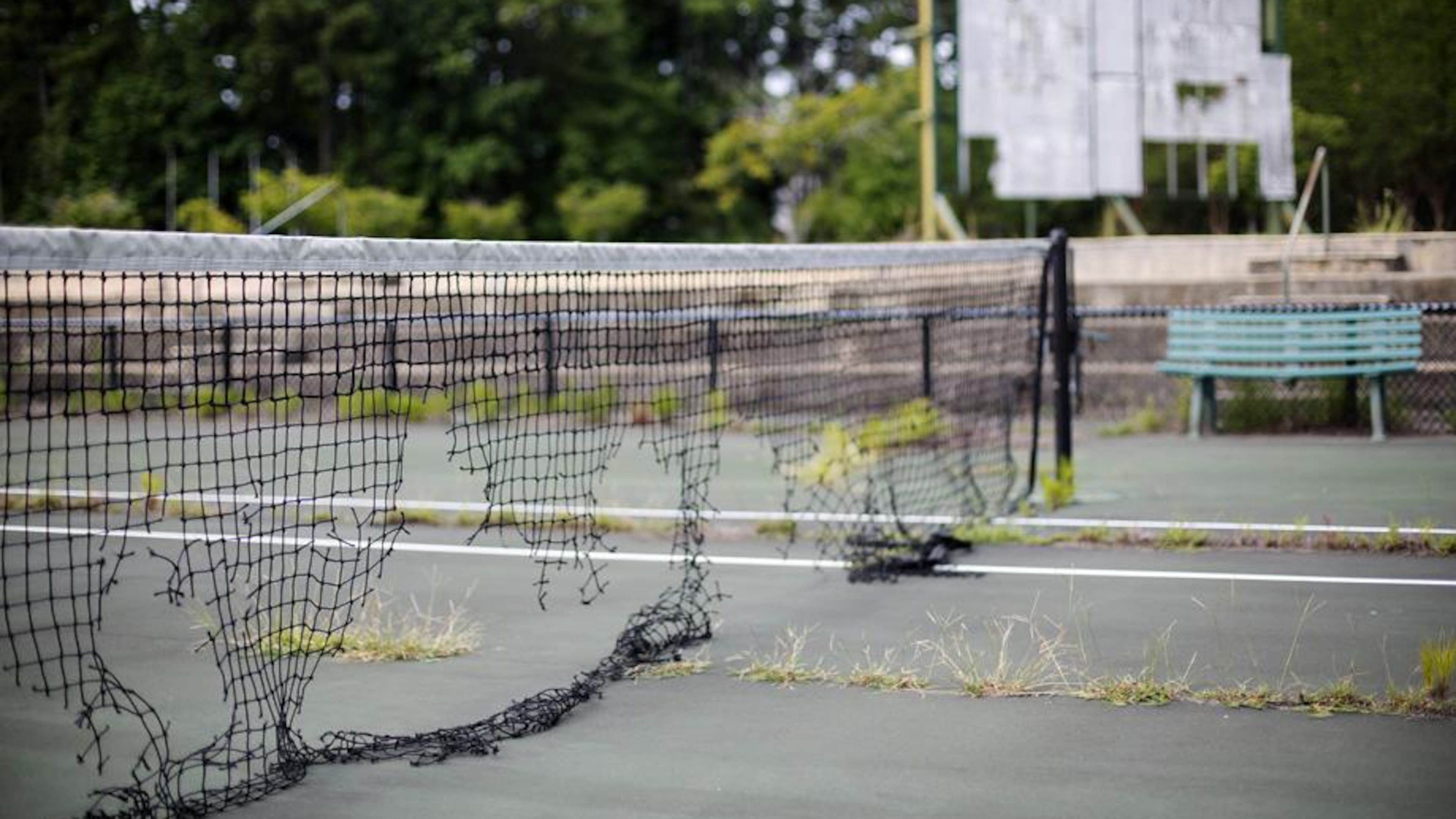 In this July 19, 2016, photo, the derelict netting and scoreboard in the background on a tennis court stand at the Stone Mountain Tennis Center, home of the 1996 Summer Olympic Games tennis events, in Stone Mountain, Ga. The permanent tennis facility built in a corner of Stone Mountain Park quickly became a money loser and now sits idle, weeds growing through the outer courts and the scoreboard in disrepair. (AP Photo/David Goldman)