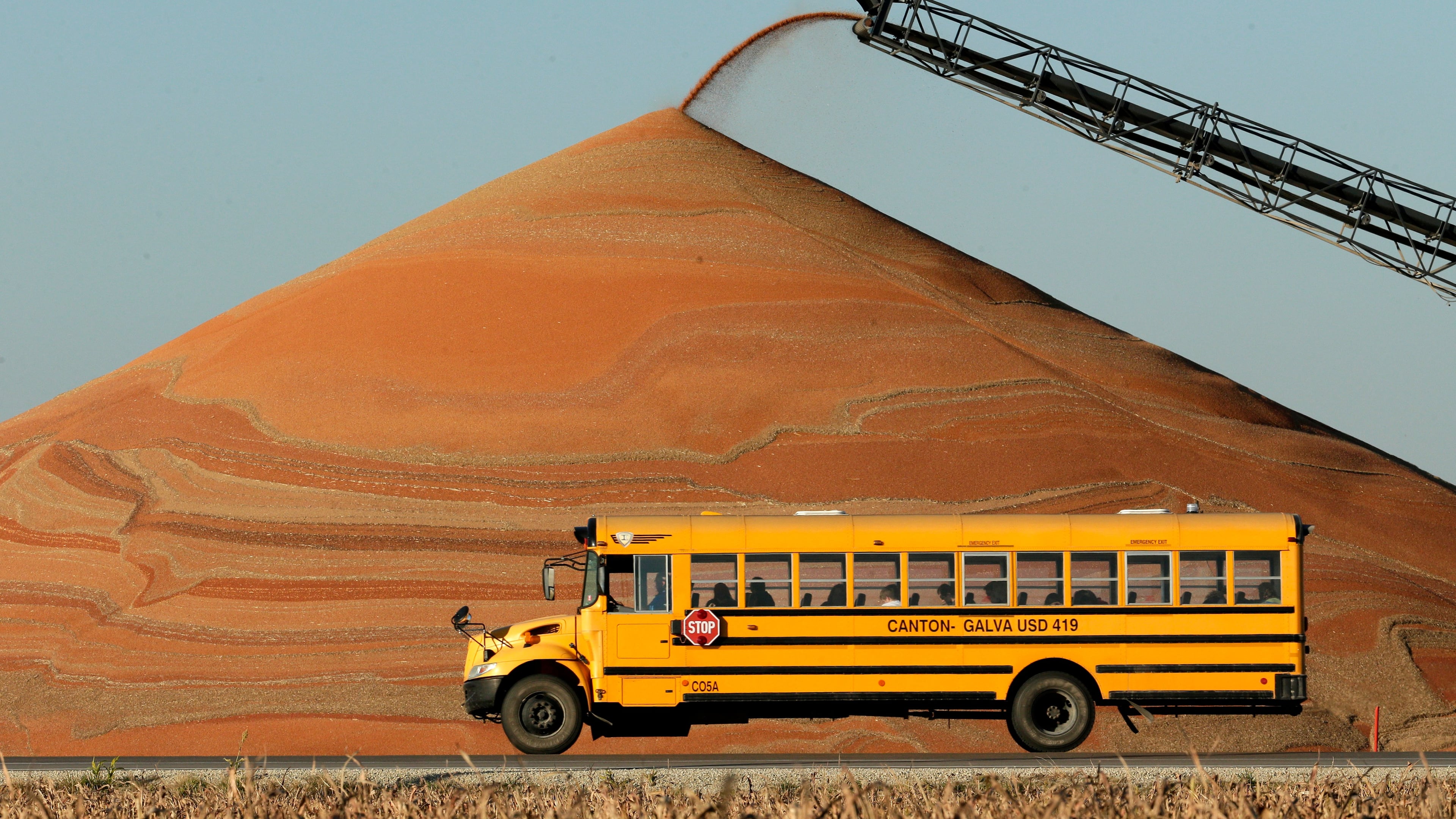 FILE - A school bus passes a pile of milo at a grain storage facility near Canton, Kan., Nov. 10, 2015. (AP Photo/Charlie Riedel, File)