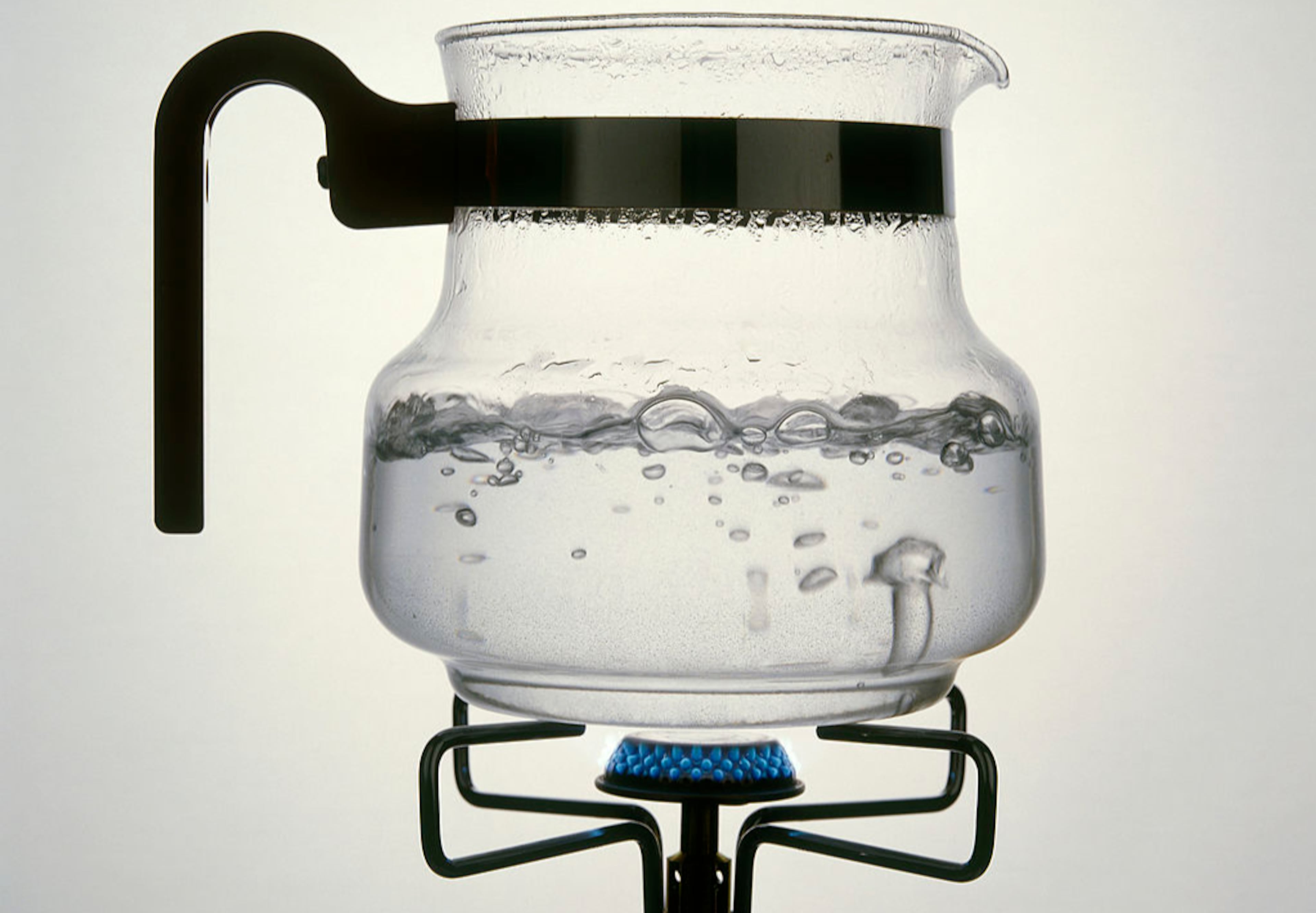 A photo of water boiling in a glass carafe on a gas ring.
