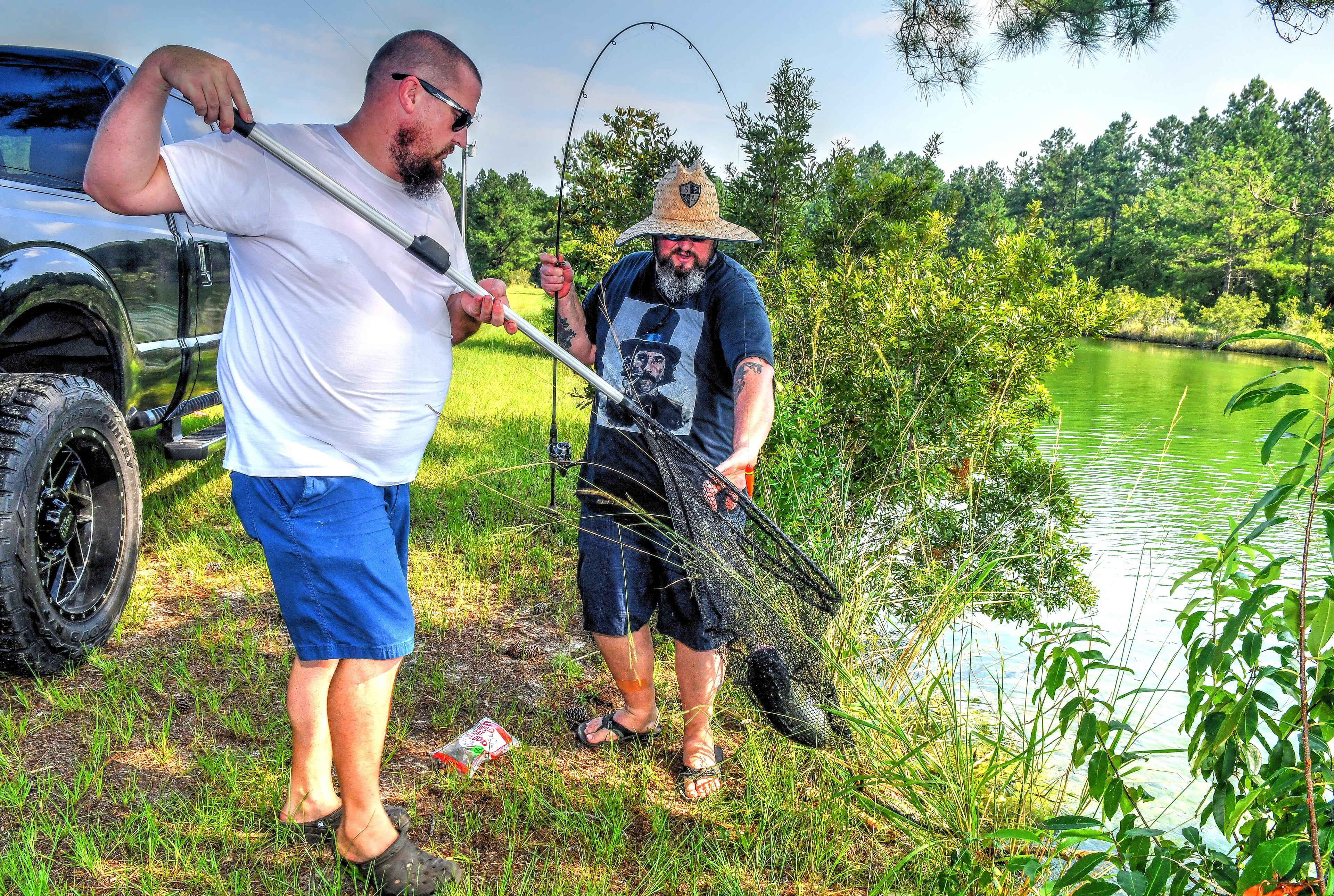 210801 White Oak, Ga.: Eric Miller, Satilla Ponds farm operator (left) helps Tim Lensch, executive chef at Georgia Sea Grill, land a large catfish that gave Lensch a tough battle along the shore of one of the ponds Sunday morning. Photo made at Satilla Ponds. Photos for Georgia on my Plate series, where we visited the 2 farms owned by Zack Gowen, who also owns the Georgia Sea Grill on Saint Simons Island. His farms (Satilla Ponds and Potlikker Farm) provide fresh fish and vegetables for the restaurant. Photos taken Sunday August 1, 2021. (Chris Hunt for The Atlanta Journal-Constitution)
