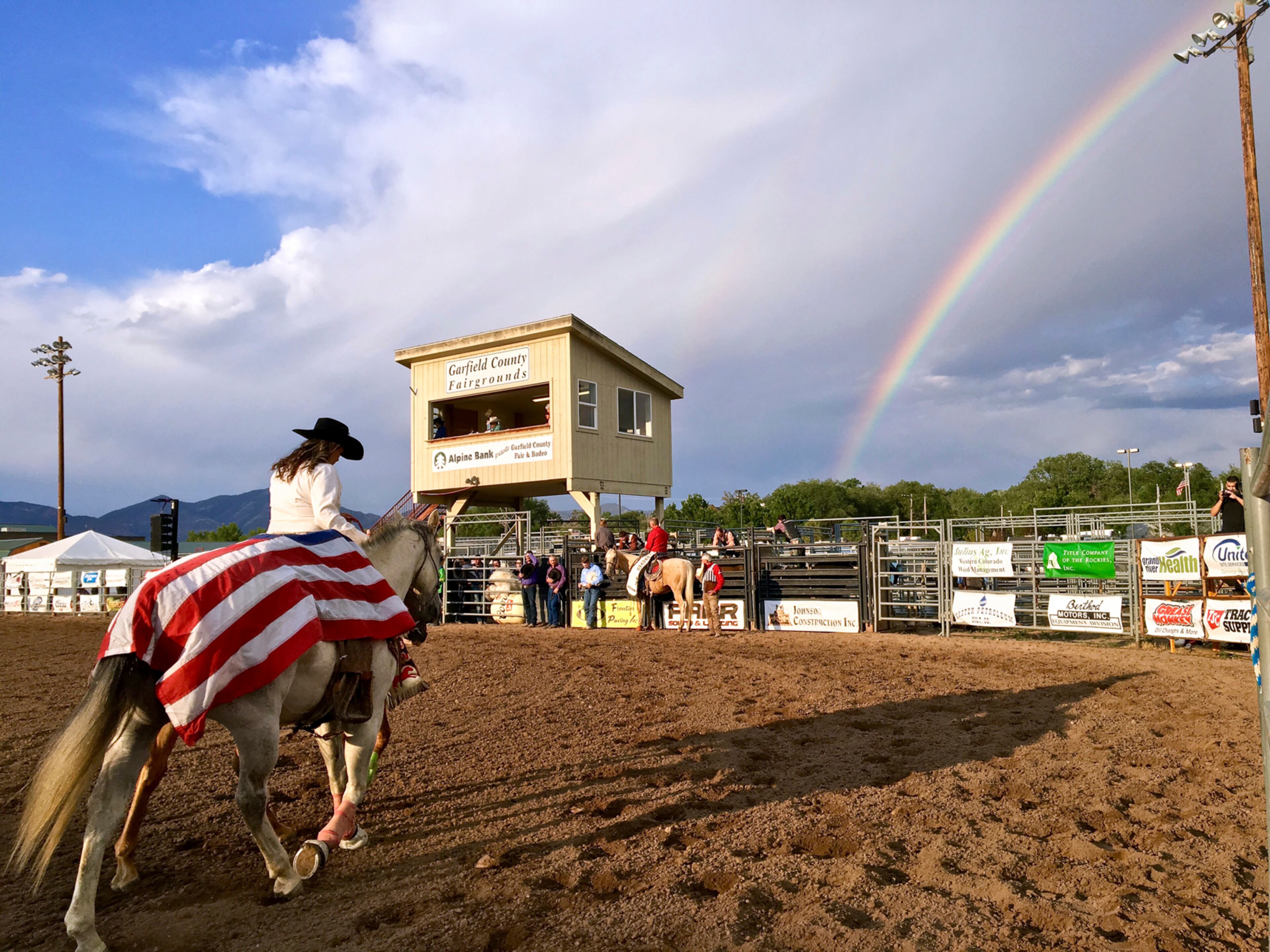 In this Wednesday, Aug. 2, 2017 photo, a flag-draped riderless horse to honor the fallen is led at the Garfield County Fair and Rodeo as a rainbow appears in Rifle, Colo. (Chelsea Self/Glenwood Springs Post Independent via AP)