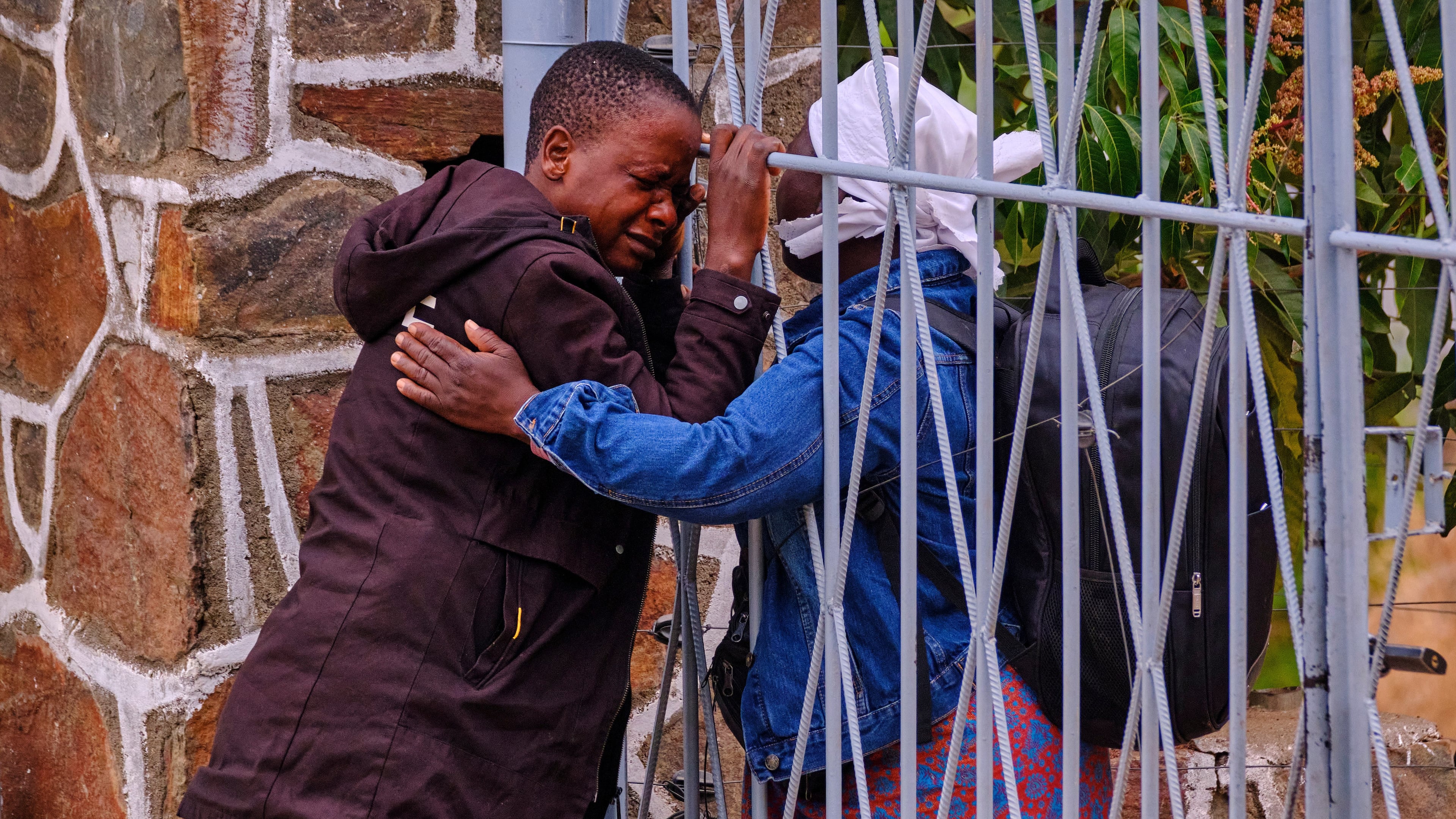Philis Hamandise, center, is embraced through a gate by a colleague at a victim identification center after losing her 9-year-old daughter and 6-year-old nephew in a ferry capsizing on Lake Kariba, in Kariba, Zimbabwe, Thursday, Aug. 13, 2026. (AP Photo/Mkhululi Thobela)