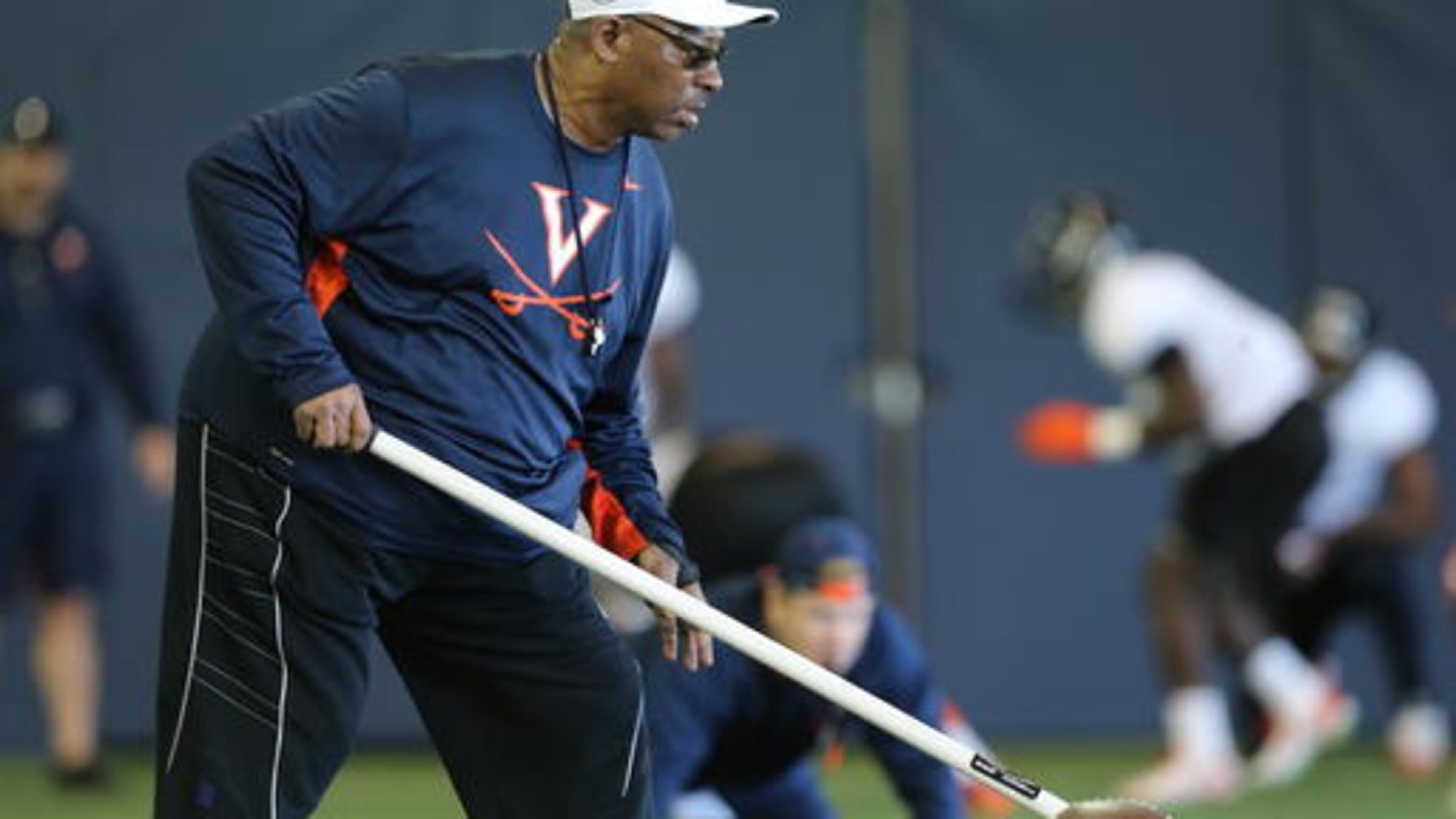 In this March 29, 2016 photo provided by the University of Virginia, assistant head coach Ruffin McNeill works with players during a team practice in Charlottesville, Va. McNeill no longer has the big corner office, and he says thay's fine with him. (Jim Daves/Univ. of Virginia via AP)