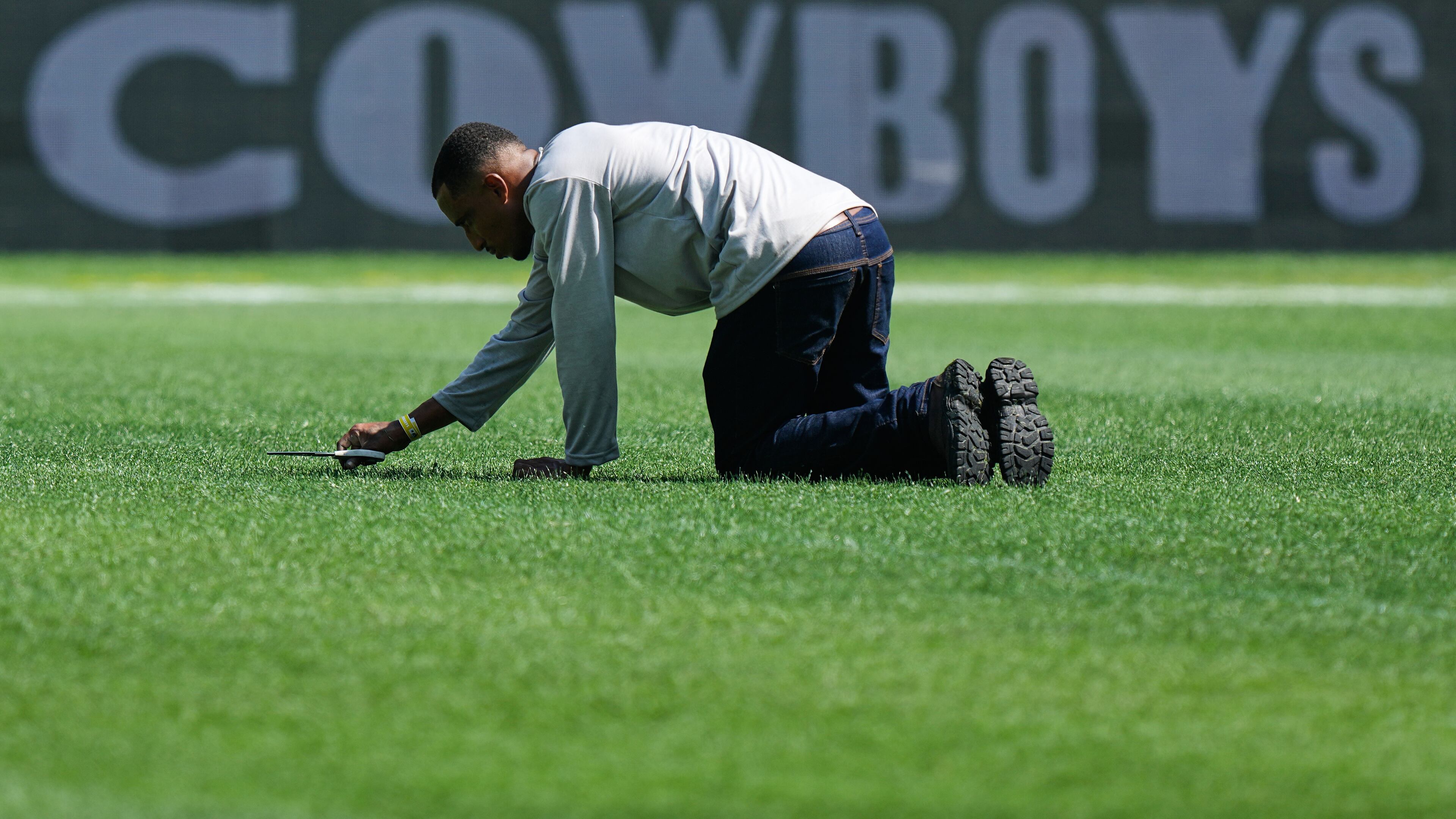 A worker cuts grass with scissors on the field ahead of an NFL football game between the Dallas Cowboys and the Baltimore Ravens in Rio de Janeiro, Saturday, Sept. 26, 2026. (AP Photo/Fernando Llano)