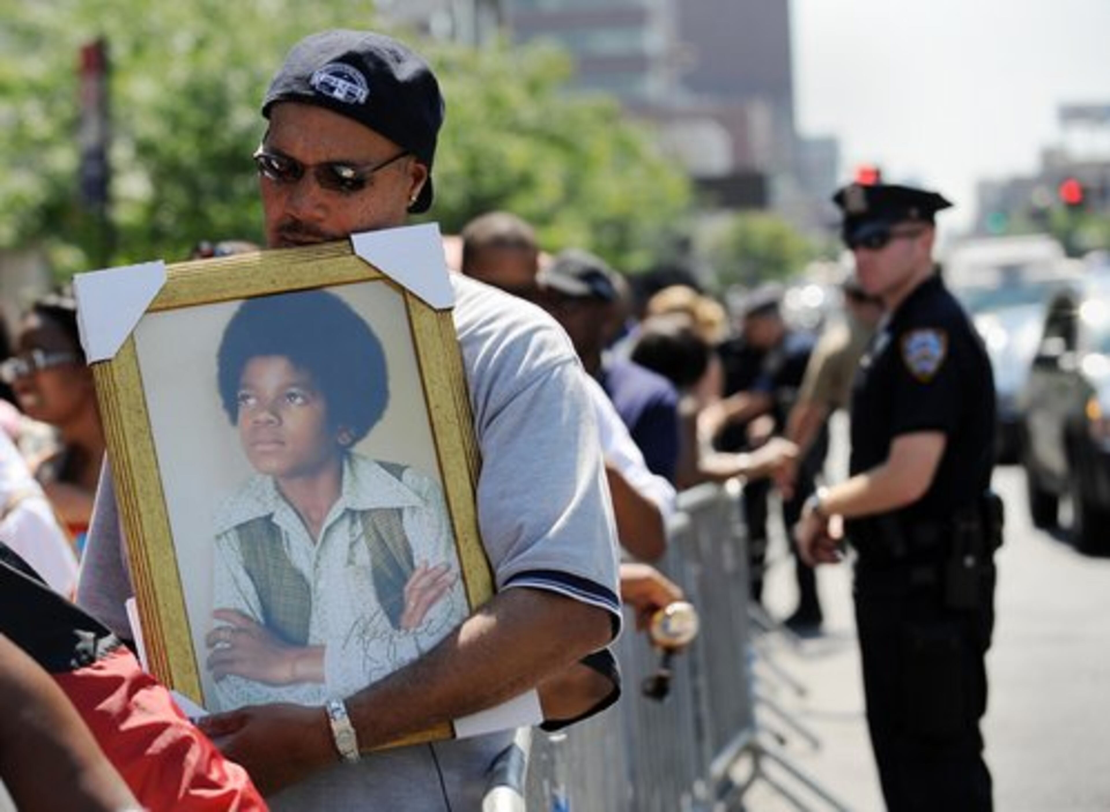 Michael Townes holds a portrait of a young Michael Jackson as he and other people wait in line.
