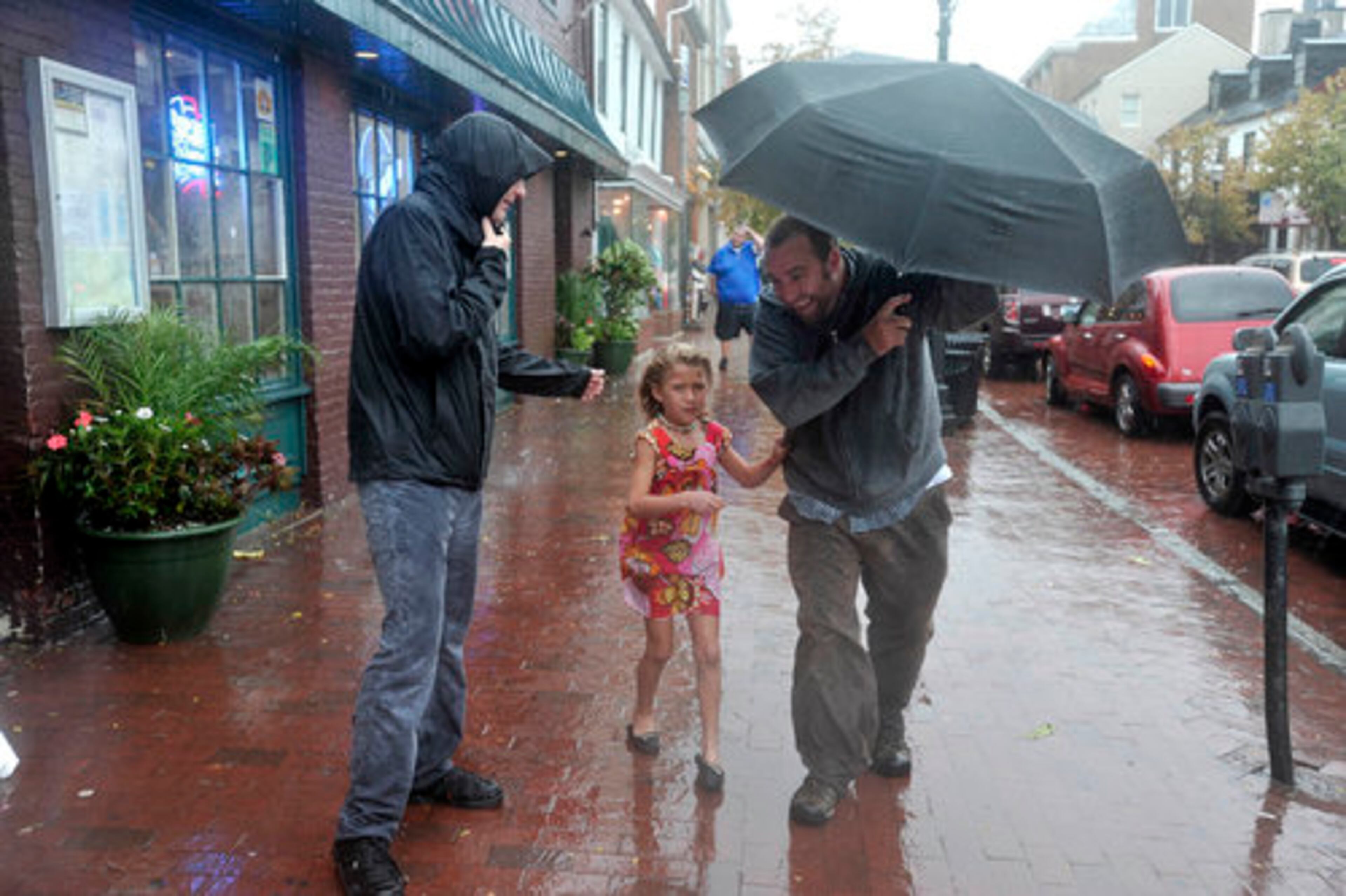 Left to right, Bobby Edds, Madilyn O'Neil, 6, and her father, Mike O'Neil, all of Annapolis, Maryland, walk on Main Street in Annapolis, as the rain and wind in advance of Hurricane Irene increases, Saturday, August 27, 2011. They checked on a friend in a nearby business and had lunch.