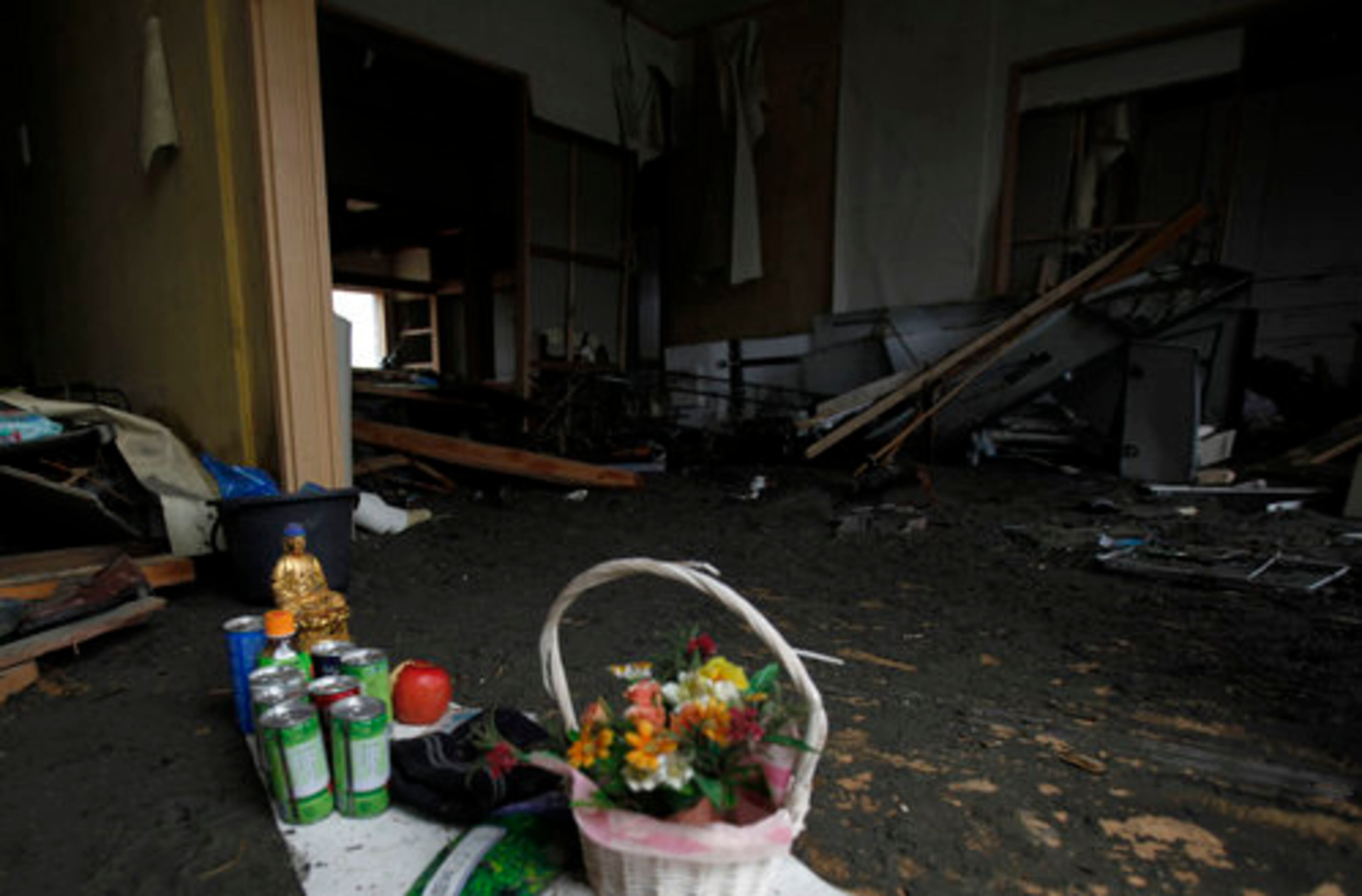 A small Buddha statue is placed with flowers and canned juices, supposed to be a makeshift altar for a victim, at a house destroyed by an earthquake and tsunami in Minamisanriku, Miyagi Prefecture.