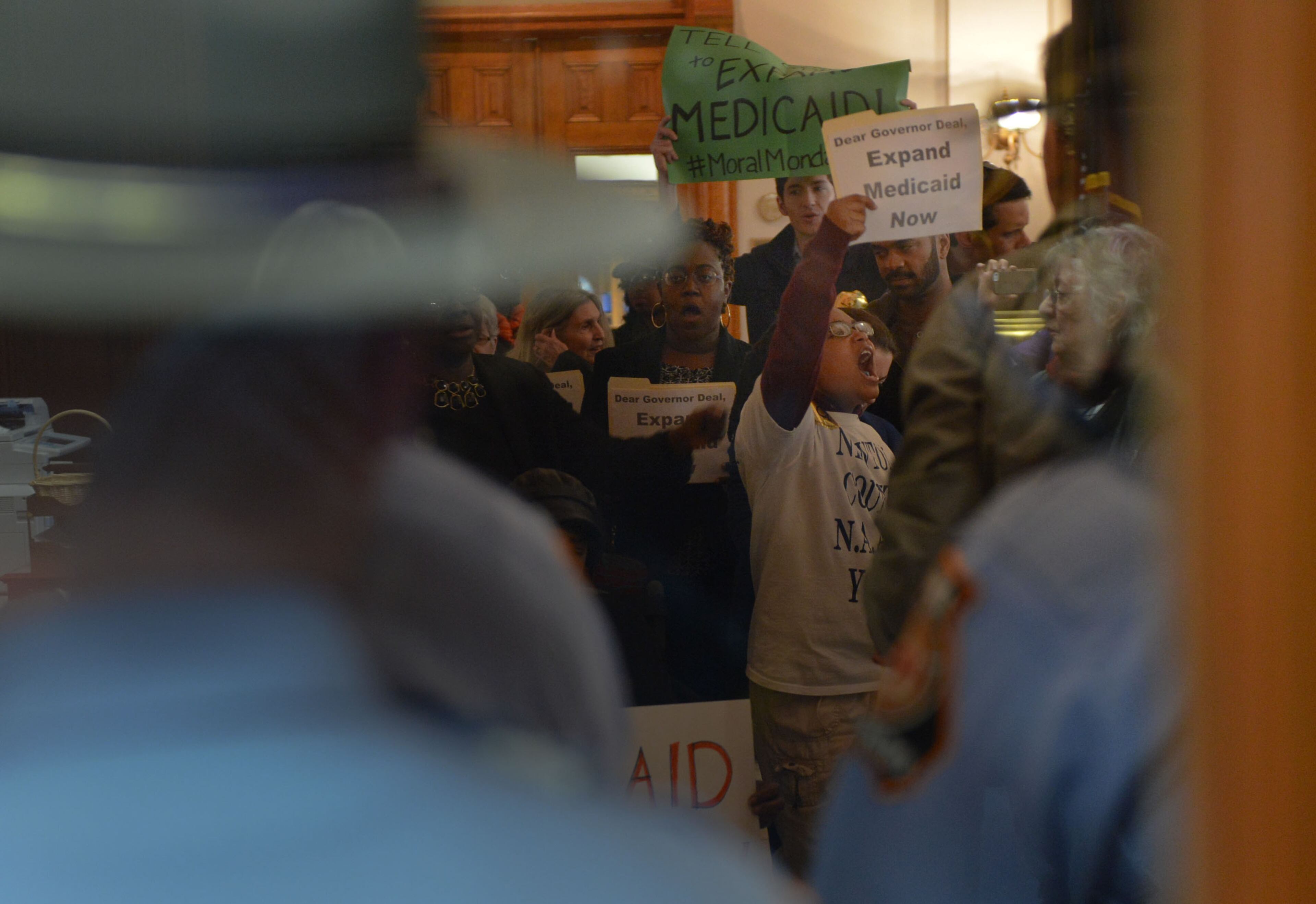 Protesters outside Gov. Nathan Deal's office are seen through Georgia State Patrol troopers manning the doorway. Ten protesters, including State Sen Vincent Fort, were arrested in the Governor's Office shortly after 5 p.m. Monday, January 27, 2014. KENT D JOHNSON/KDJOHNSON@AJC.COM
