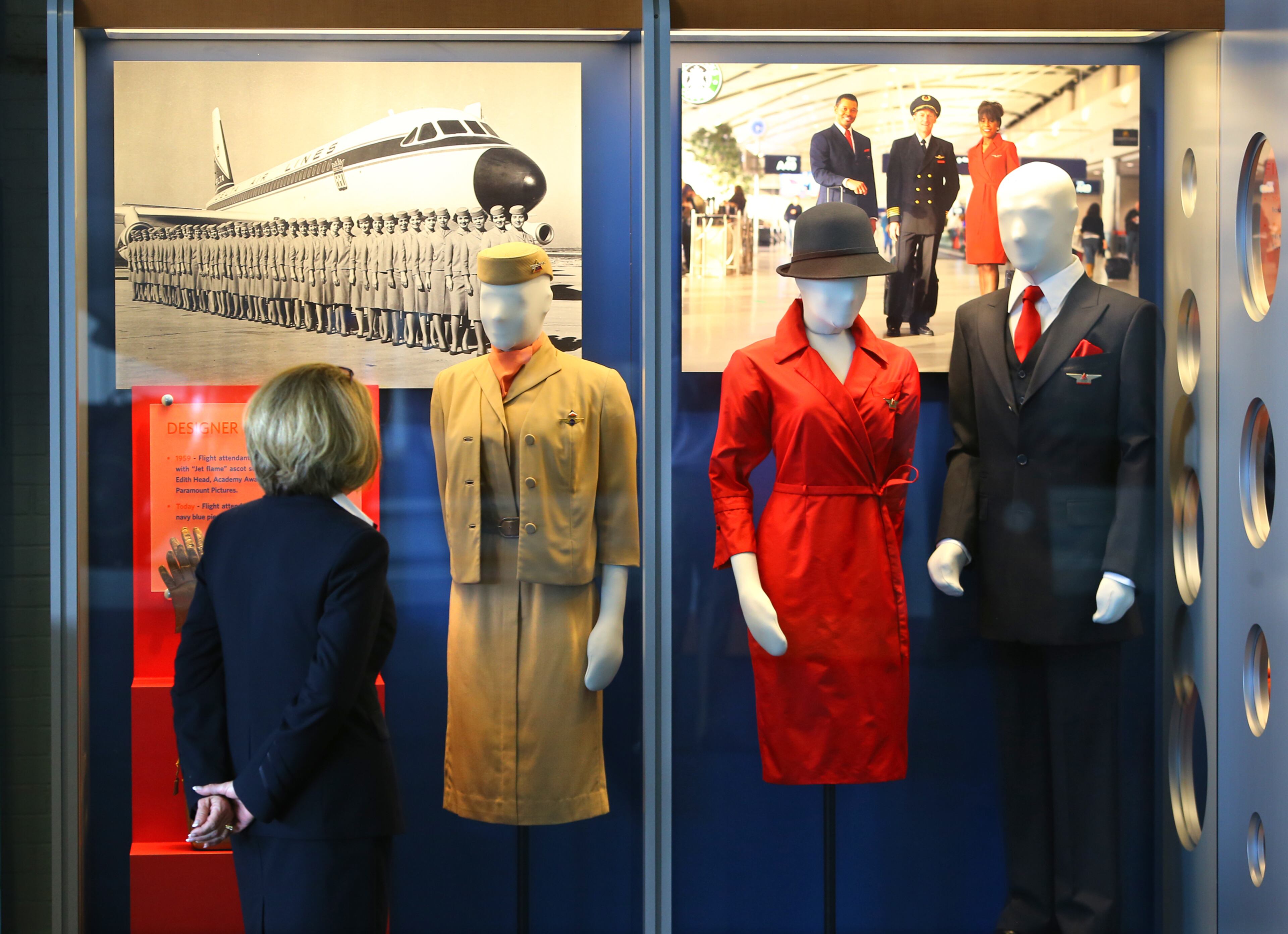 061214 ATLANTA: Delta flight crew member Karen Januszewski takes in a display of designer uniforms including a 1959 accessorized uniform with "Jet flame" ascot scarf that were designed by Academy Award-winning Paramount Pictures chief designer Edith Head (at left) and today's flight attendant uniforms of iconic red drresses and navy blue pieces designed by Richard Tyler in 2006 at the Delta Flight Museum on Thursday, June 12, 2014, in Atlanta. CURTIS COMPTON / CCOMPTON@AJC.COM