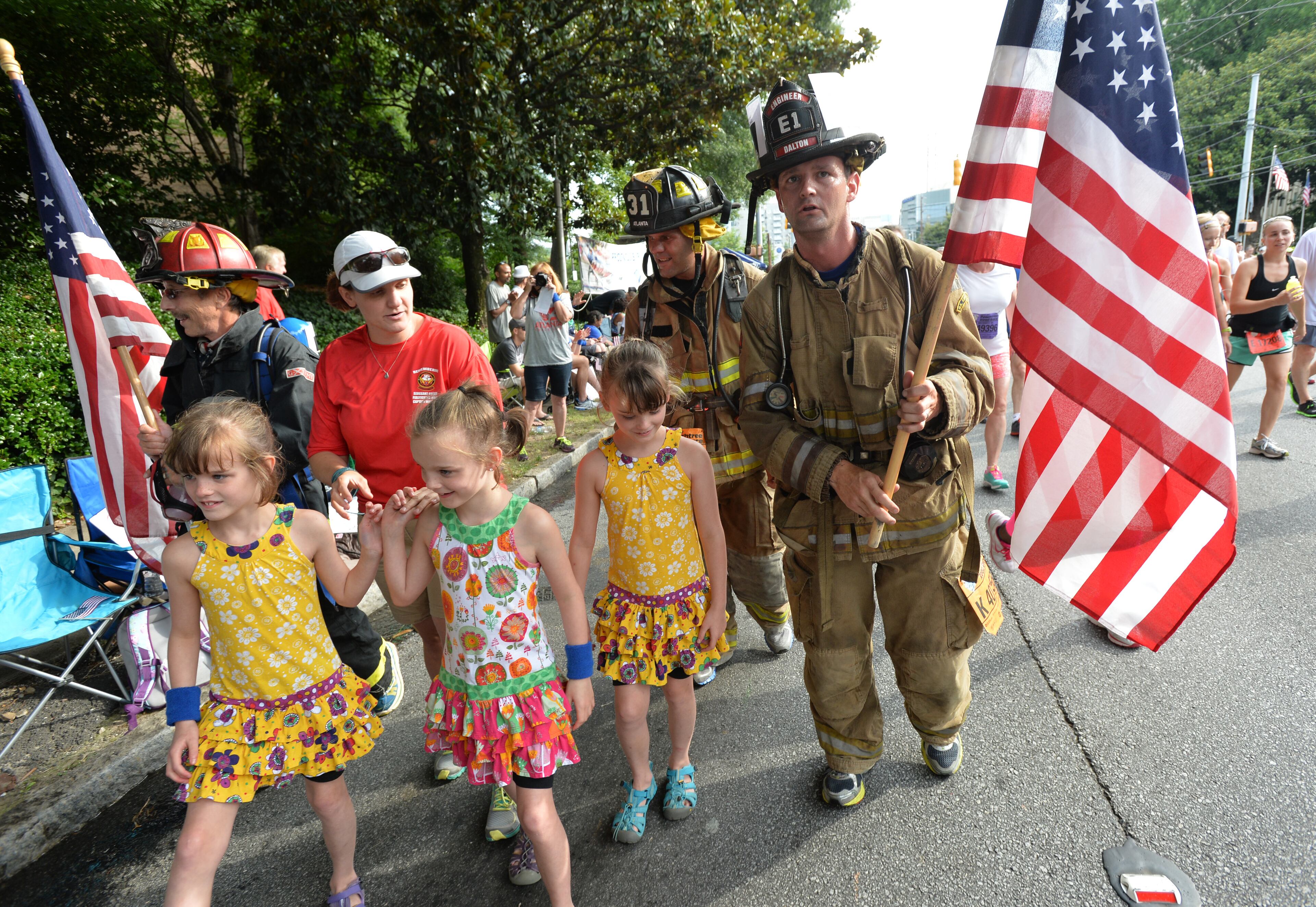 July 4, 2014 Atlanta - Firefighters (from left) Johnny Buice, Kris Peringer, Doulas Kerns walk with family members of Frank Guinn, who was killed after being hit by a car just before the New Orleans Ironman race, wife Kimberly Guinn with her triplets (from left) Issy, Alyssa, and Makenna, all of 7, near The Shepherd Center during the 2014 AJC Peachtree Road Race on Saturday morning, July 4, 2014. HYOSUB SHIN / HSHIN@AJC.COM
