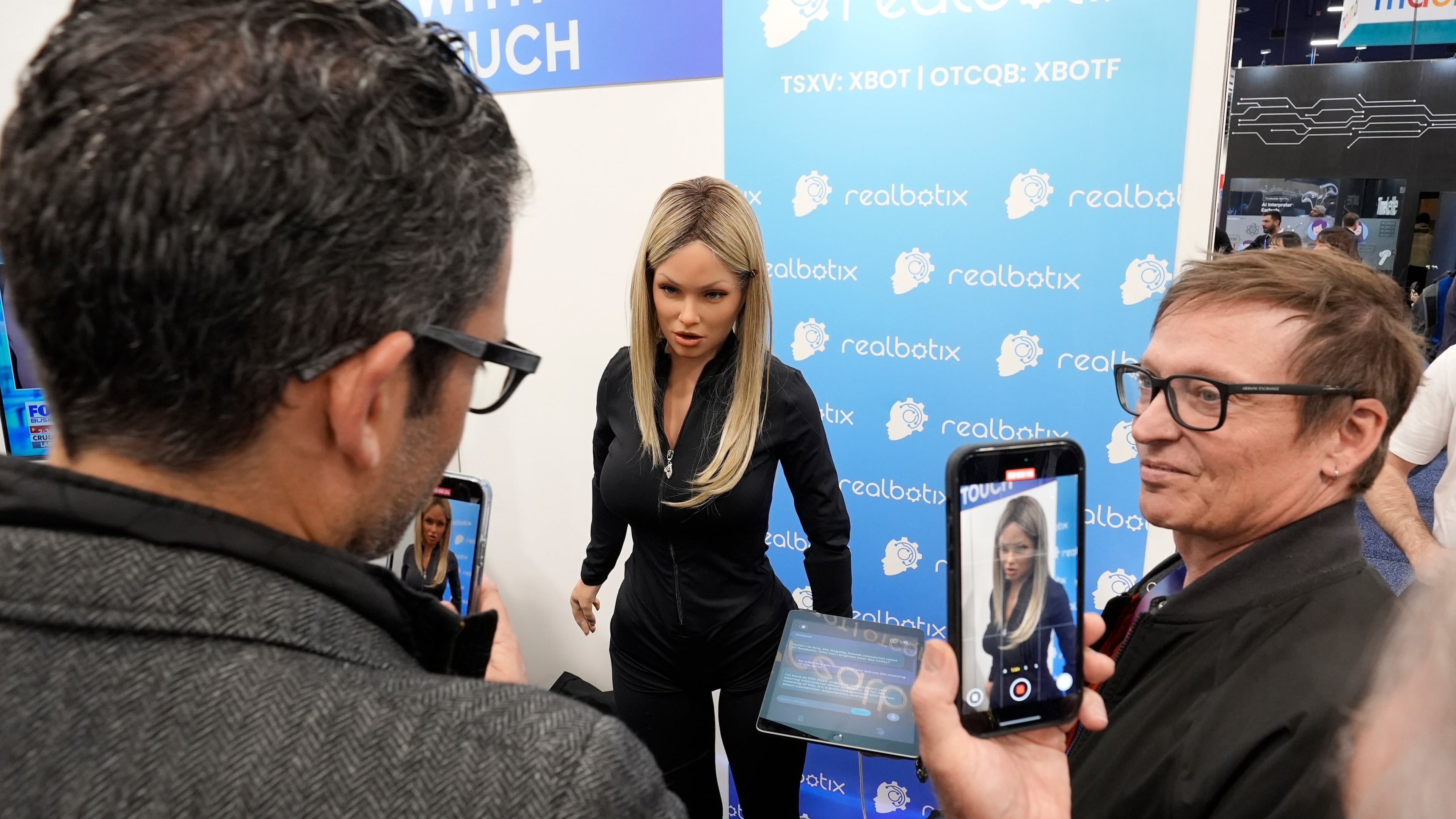FILE - A Realbotix humanoid robot, center, speaks with attendees at a Realbotix booth during the CES tech show Jan. 8, 2025, in Las Vegas. (AP Photo/Abbie Parr, File)