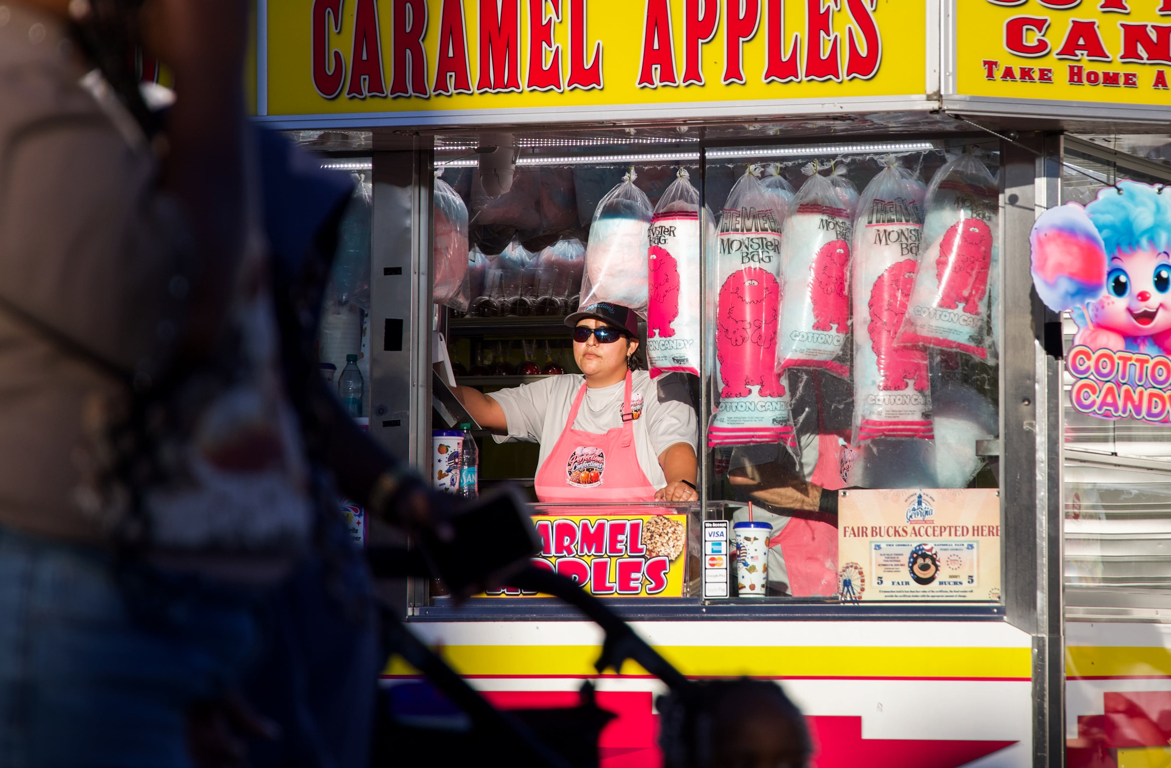 Belkis Deaz waits for customers at the Perfect Confections stand at the Georgia National Fair in Perry, Georgia, on Oct. 17, 2026. Deaz has worked at fairs for the past four years, traveling all around the country. (Emily Laycock/UGA Photojournalism Workshop)