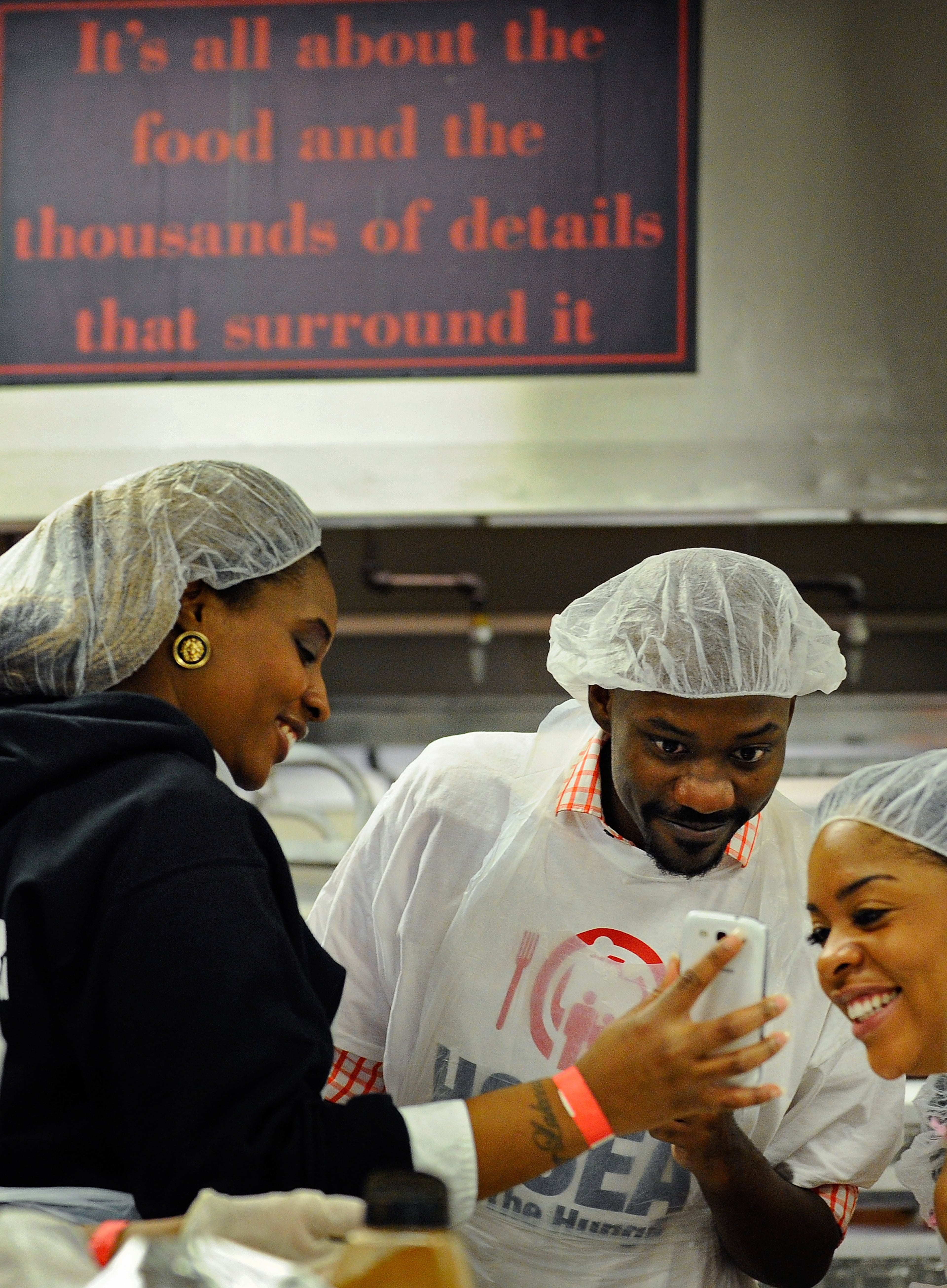 While they check out a group photo, brother and sister volunteers Lakeea Harrington, Eddie Williams and Brenda Washington, left to right, are framed by a sign in the kitchen at the Georgia World Congress Center reminding them about their mission during the annual Hosea Feed the Homeless Christmas dinner on Thursday, Dec. 25, 2014, in Atlanta. David Tulis/AJC Special