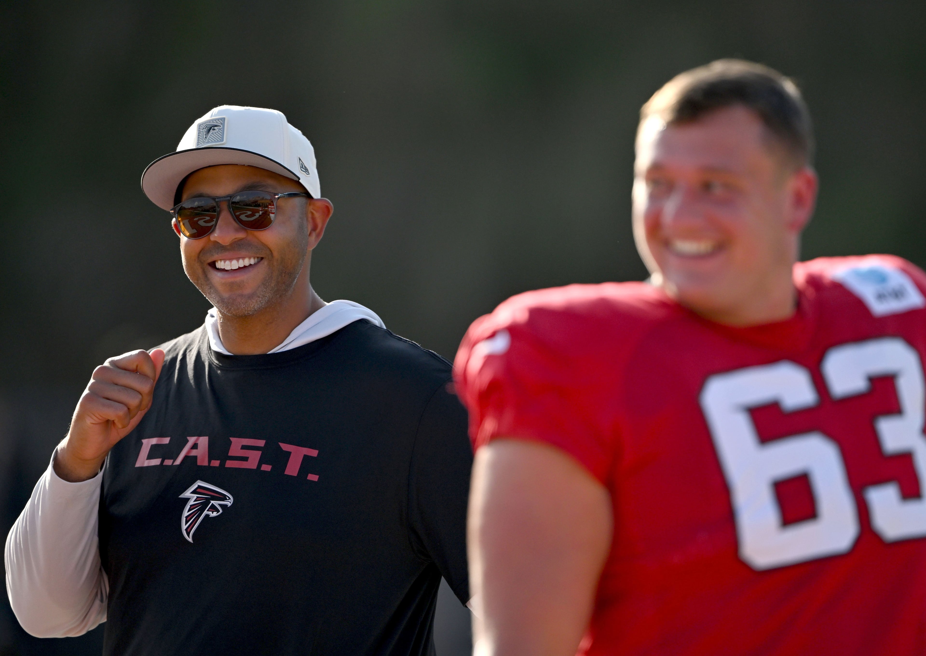 Falcons general manager Ian Cunningham (left) talks to guard Chris Lindstrom during "Saturday Night Lights" practice Saturday, Aug. 8, 2026, at Lanier High School in Sugar Hill. (Hyosub Shin/AJC)