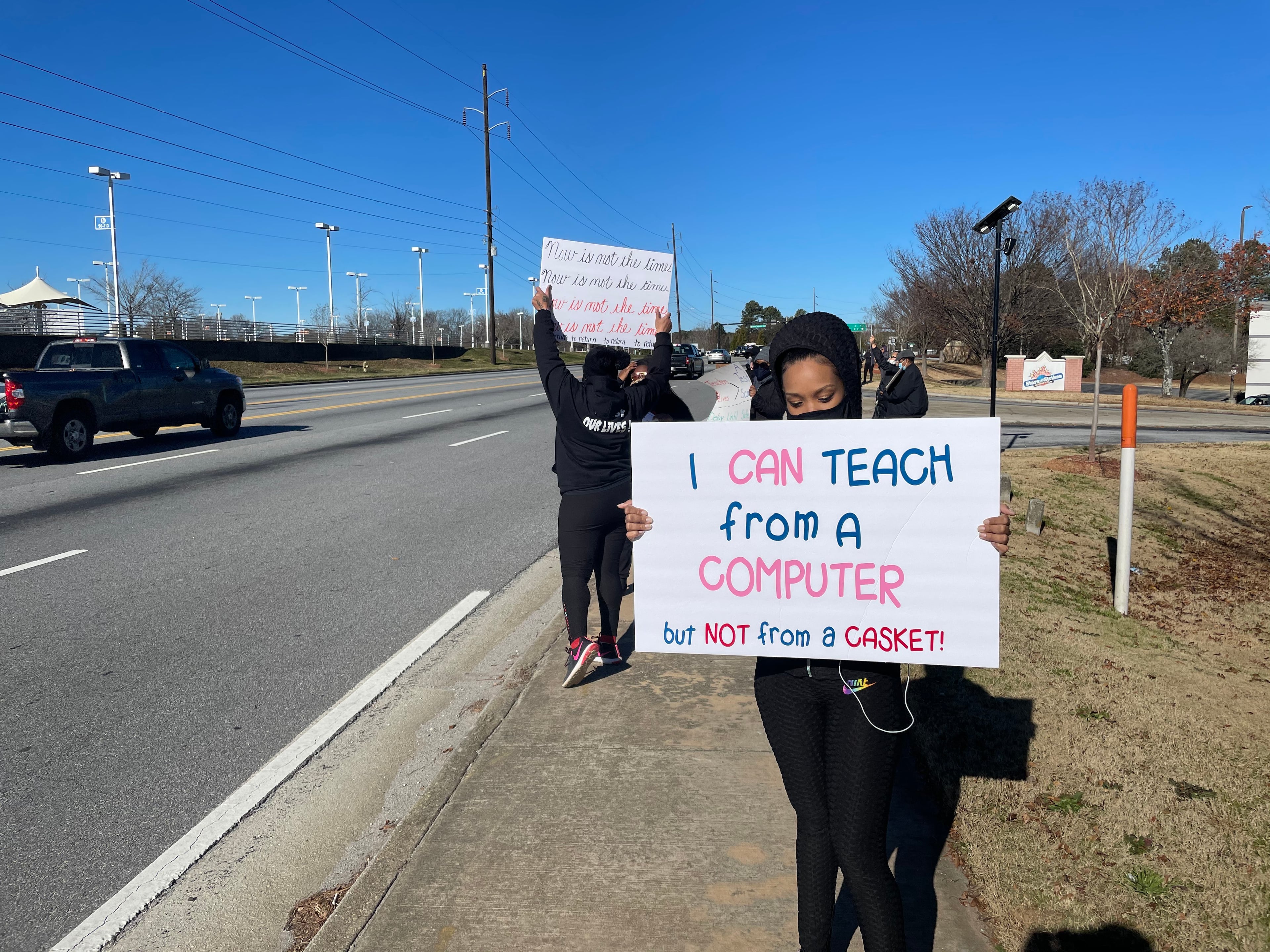 Community members in DeKalb held signs on Tuesday to protest against the reopening of DeKalb County schools.