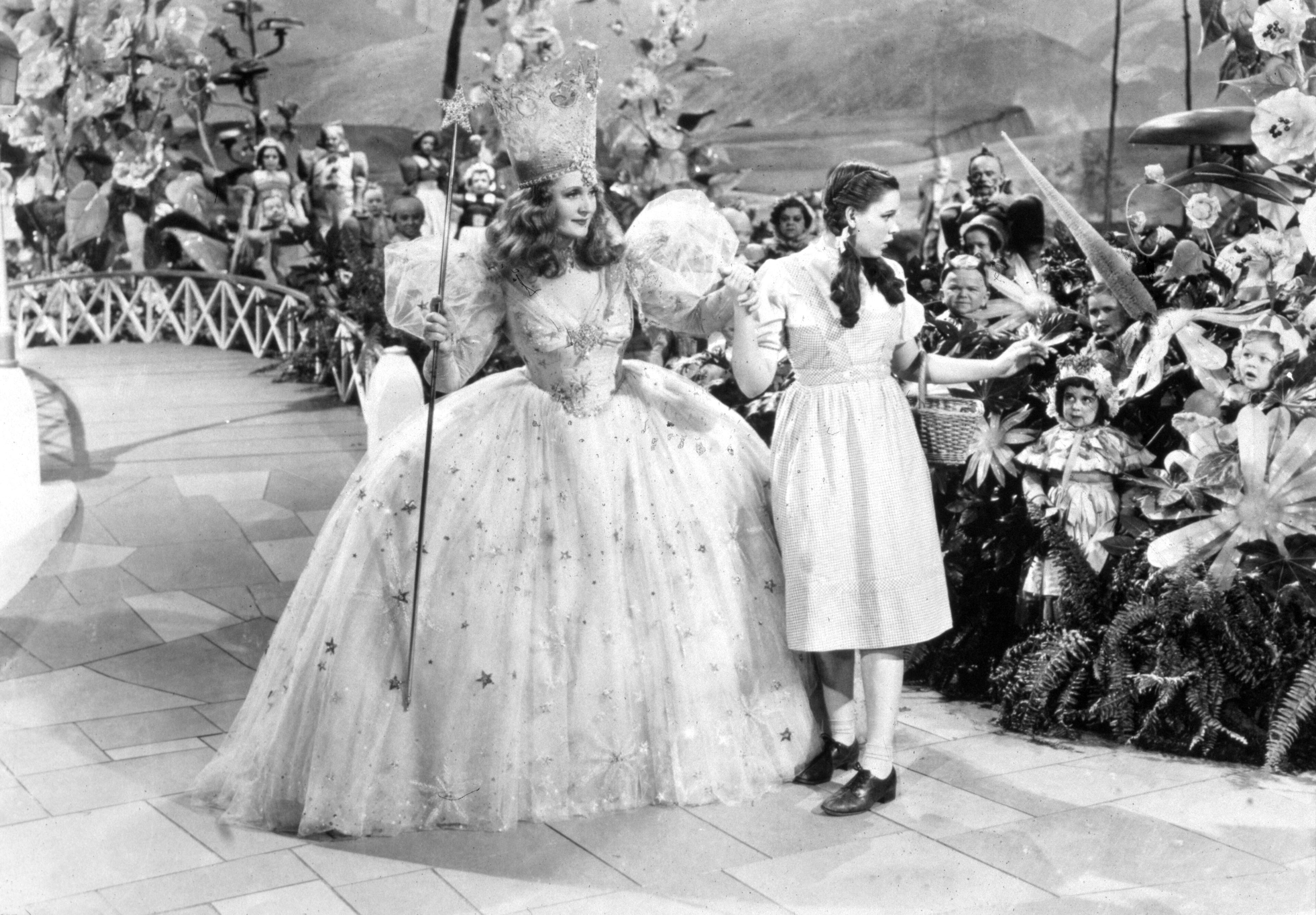 American actors Judy Garland (right) (1922 - 1969) and Billie Burke (1885 - 1970) link hands, surrounded by Munchkins in a still from the film "The Wizard of Oz,' directed by Victor Fleming, 1939. (Photo by MGM Studios/Courtesy of Getty Images)