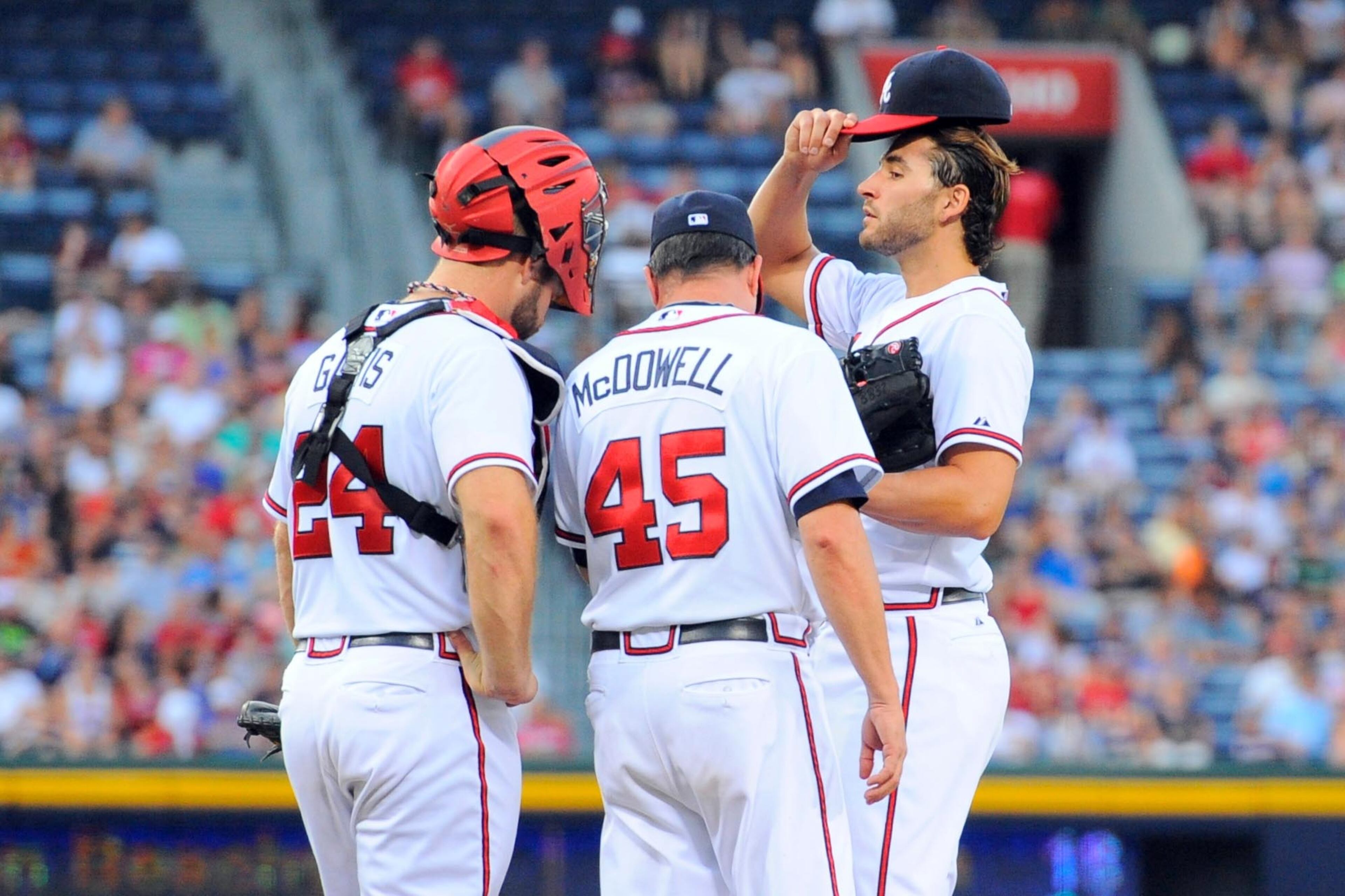 Atlanta Braves catcher Evan Gattis (24) and pitching coach Roger McDowell (45) visit with starting pitcher Brandon Beachy (37) during the third inning at Turner Field. Mandatory Credit: