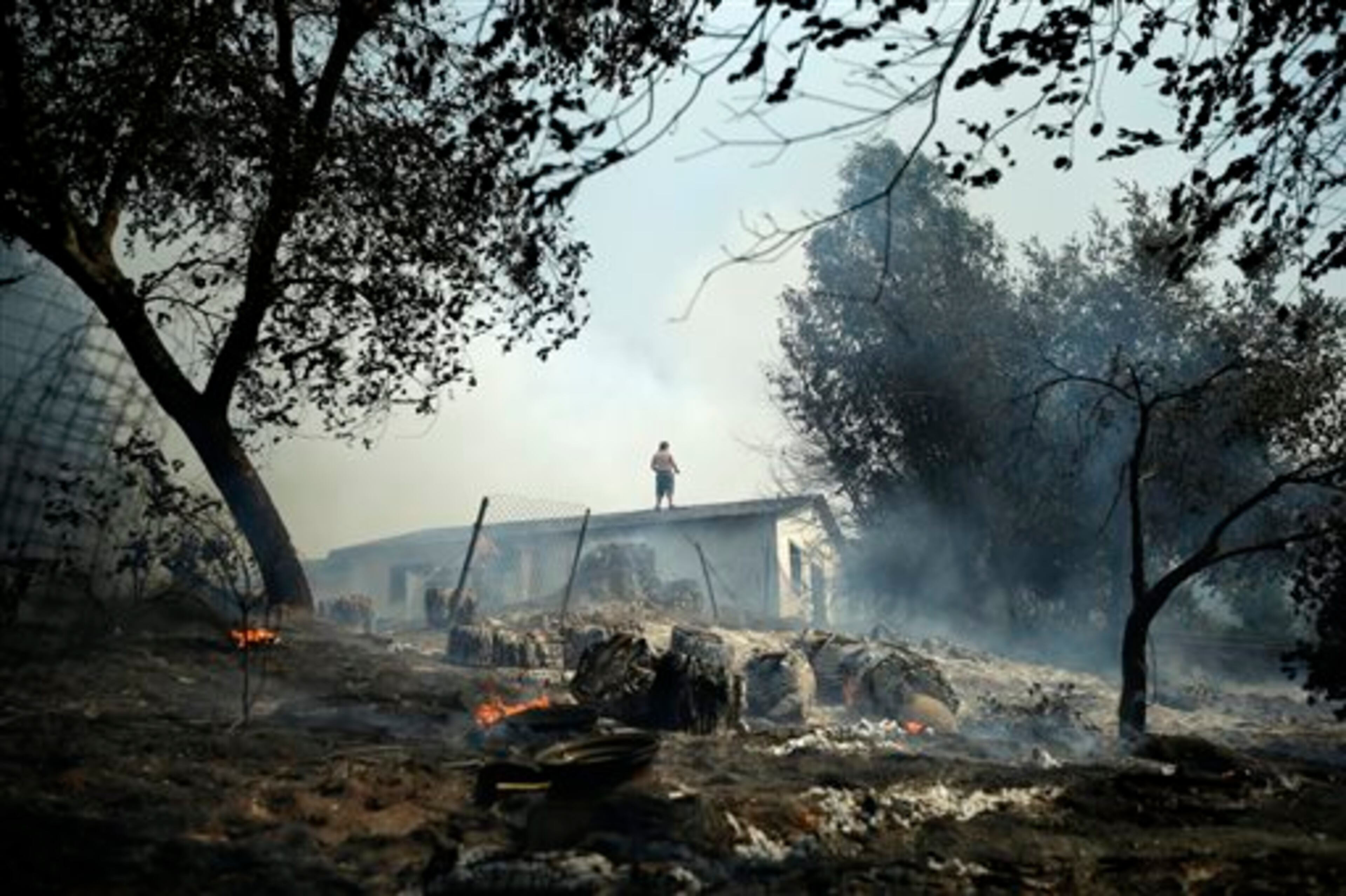 Jeff Brown waters the roof of his home as vegetation smolders during a wildfire, Thursday, May 15, 2014, in Escondido, Calif. One of the nine fires burning in San Diego County suddenly flared Thursday afternoon and burned close to homes, trigging thousands of new evacuation orders.(AP Photo/Gregory Bull)