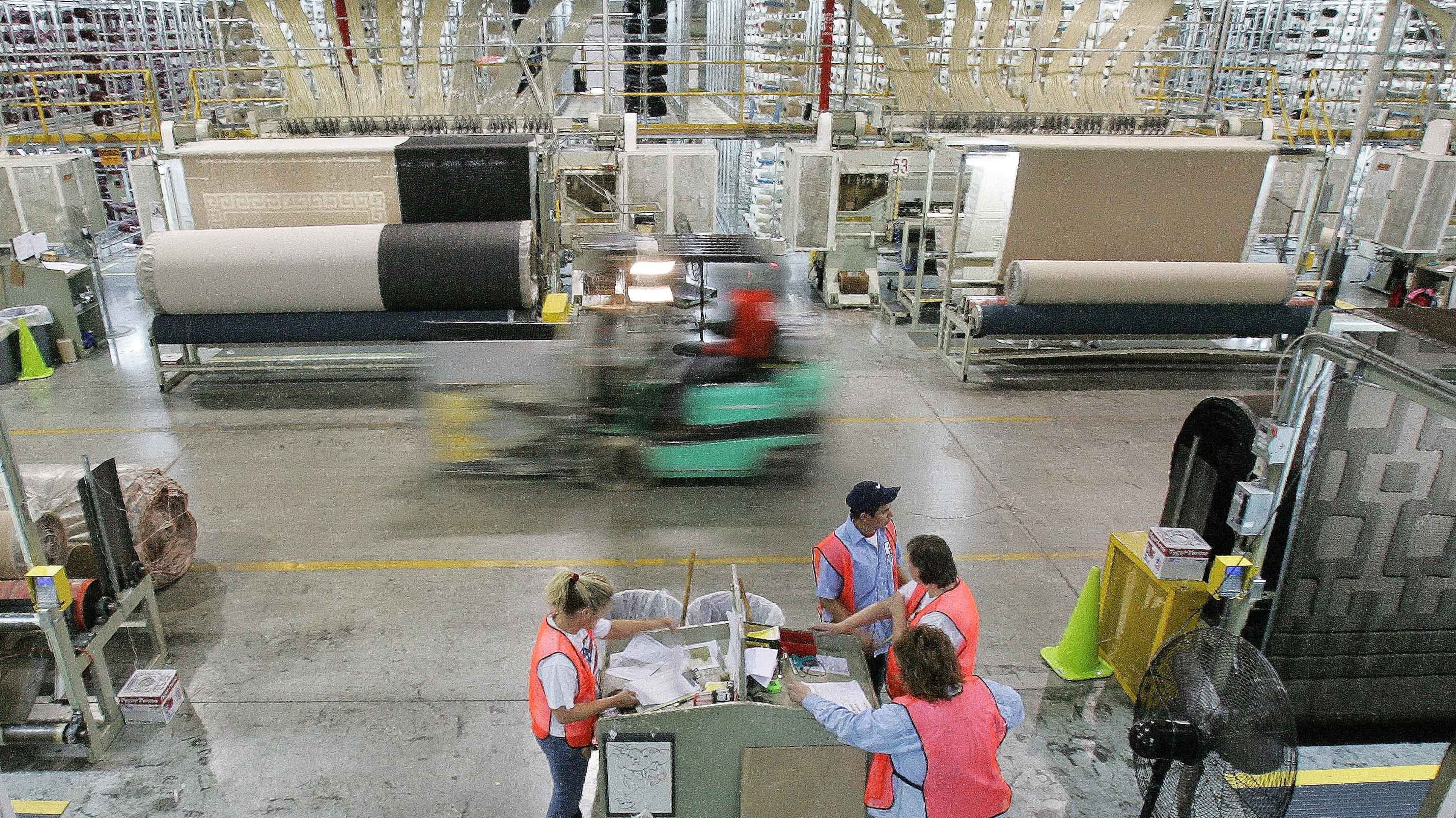 FILE - A forklift speeds by machines and workers on the production floor of a Mohawk Industries rug manufacturing plant in Calhoun, Ga., Wednesday, April 12, 2006. (AP Photo/Ric Feld, File)