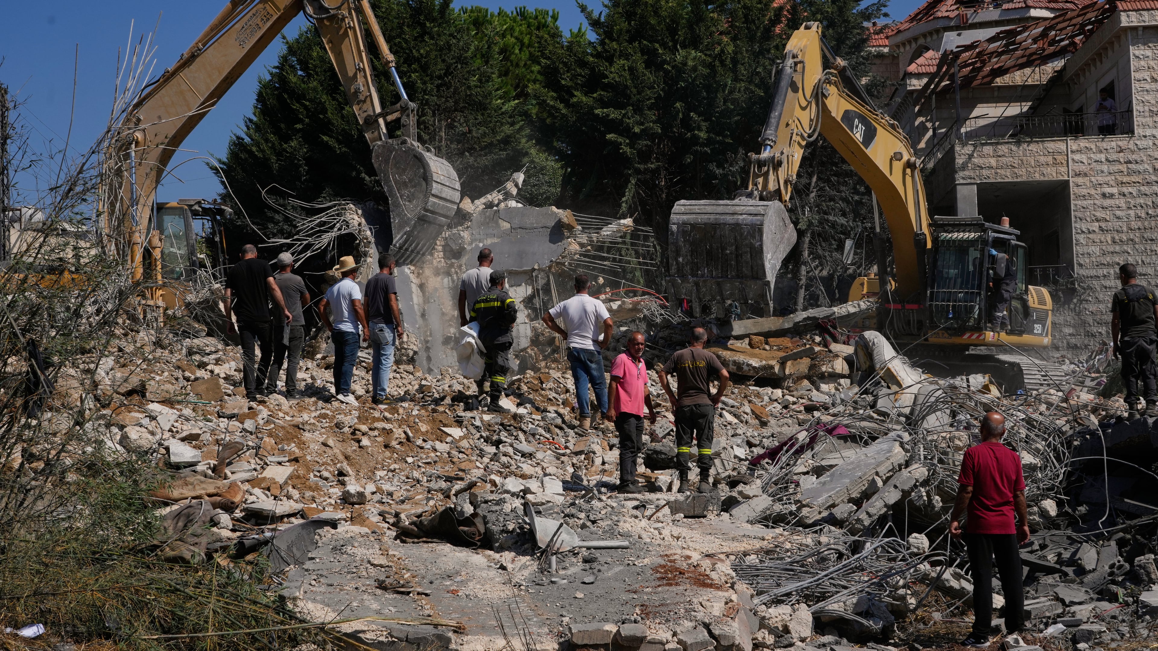 People watch rescue workers use excavators as they search for victims under the rubble of a building destroyed in an Israeli airstrike in the southern village of Kfar Rumman, Lebanon, Monday, Sept. 7, 2026. (AP Photo/Mohammed Zaatari)