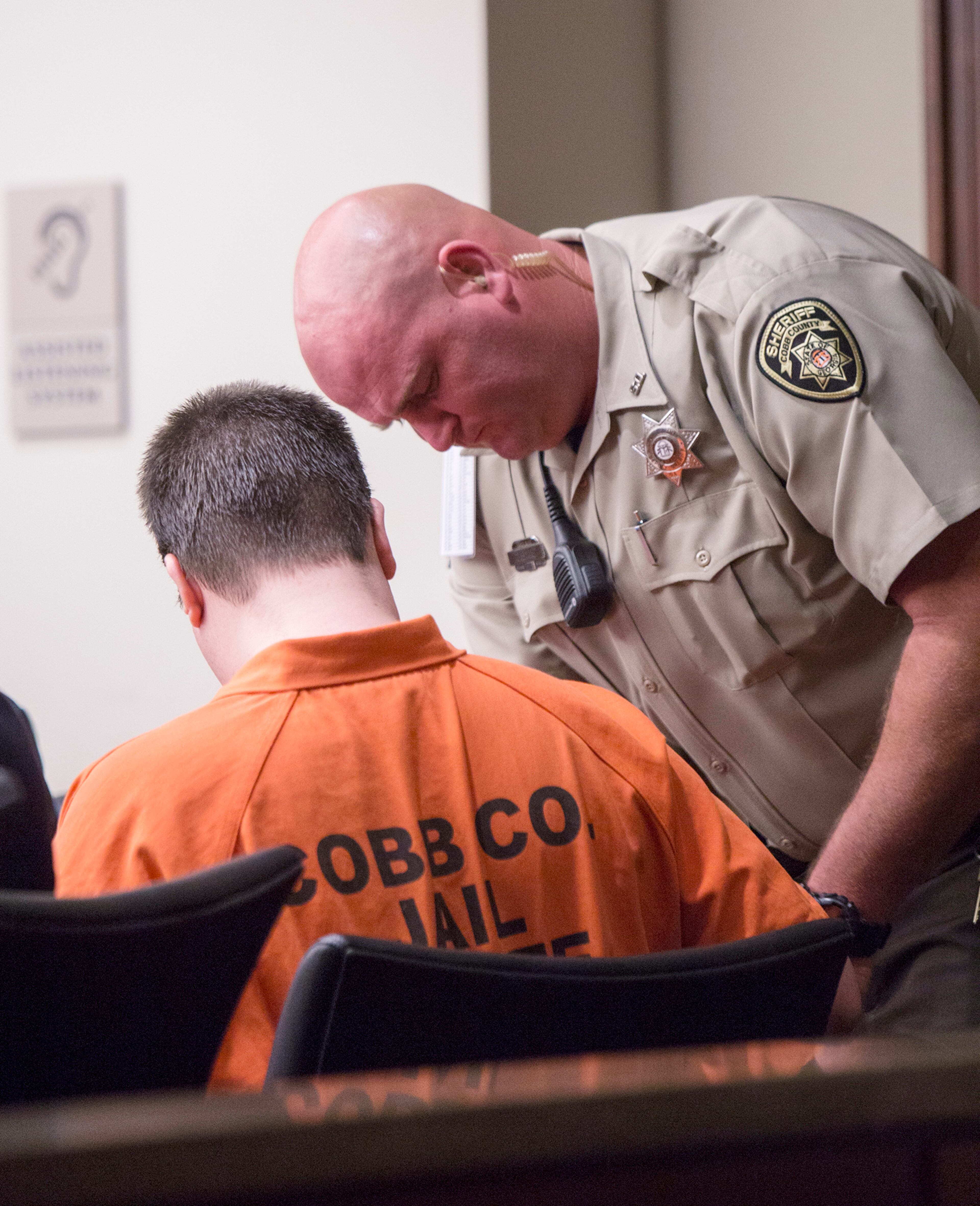 An officer unshackles one of Justin Ross Harris's arms during a hearing Monday, Sept. 14, 2015, in Marietta, Ga. A judge on Monday refused to bar the news media from the courtroom during pretrial hearings for Harris, a Georgia man accused of killing his toddler son by leaving him in a vehicle on a hot day. (Kathryn Ingall/The Marietta Daily Journal via AP, Pool)
