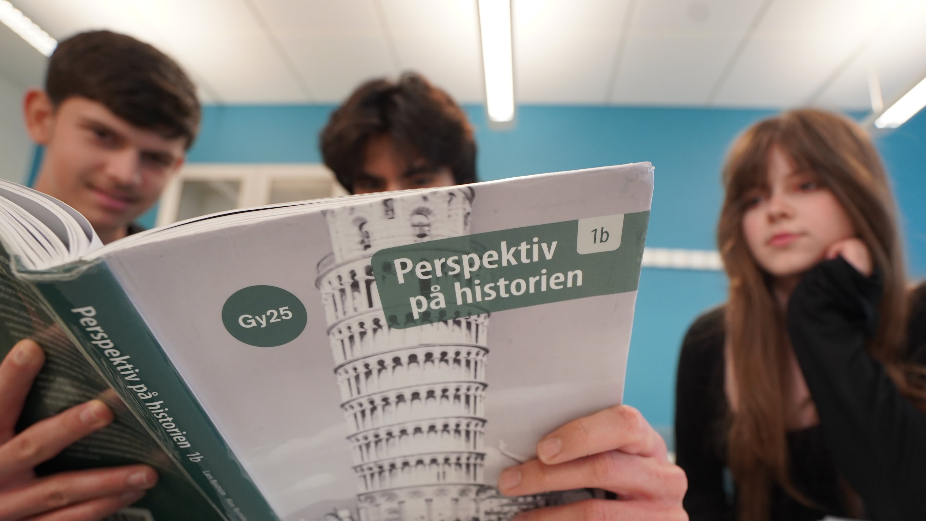 High school students from left, Vasilije Stjepanovic, Aslan Ozhan Kilicasan and Melina Sallahi pose with a history text book at Malmo Borgarskola high school in Malmo, Sweden, May 21, 2026. (AP Photo/James Brooks)