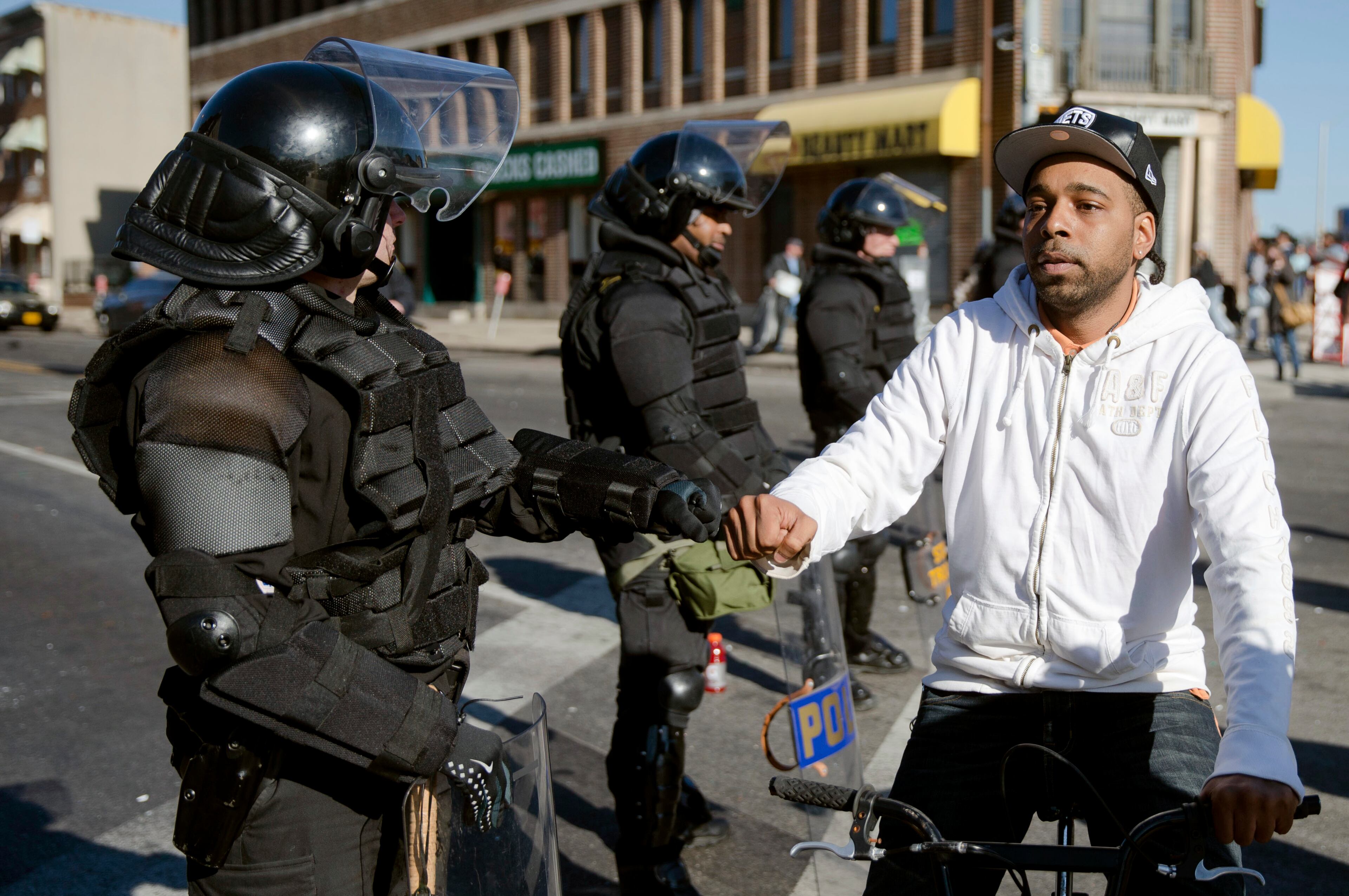 A man on a bicycle greets Maryland State Troopers Tuesday, April 28, 2015, in the aftermath of rioting following Monday's funeral for Freddie Gray, who died in police custody. The violence that started in West Baltimore on Monday afternoon had spread to East Baltimore and neighborhoods close to downtown and near Camden Yards. (AP Photo/Matt Rourke)