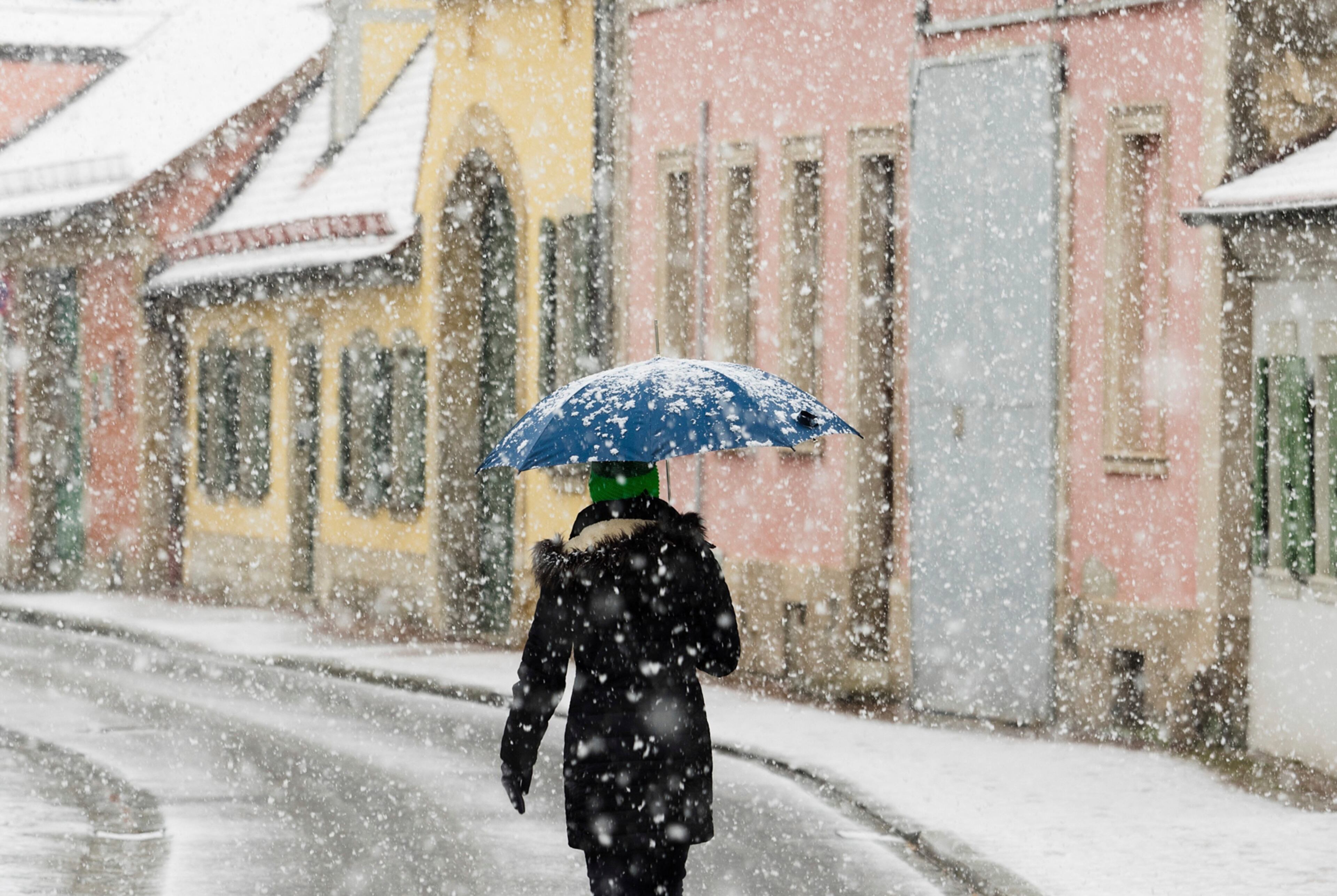A woman with umbrella walks along a street during snowfall in Bamberg, southern Germany, Easter Monday, April 17, 2017. Weather forecasts predict changeable weather and low temperatures till Wednesday. (Nicolas Armer/dpa via AP)