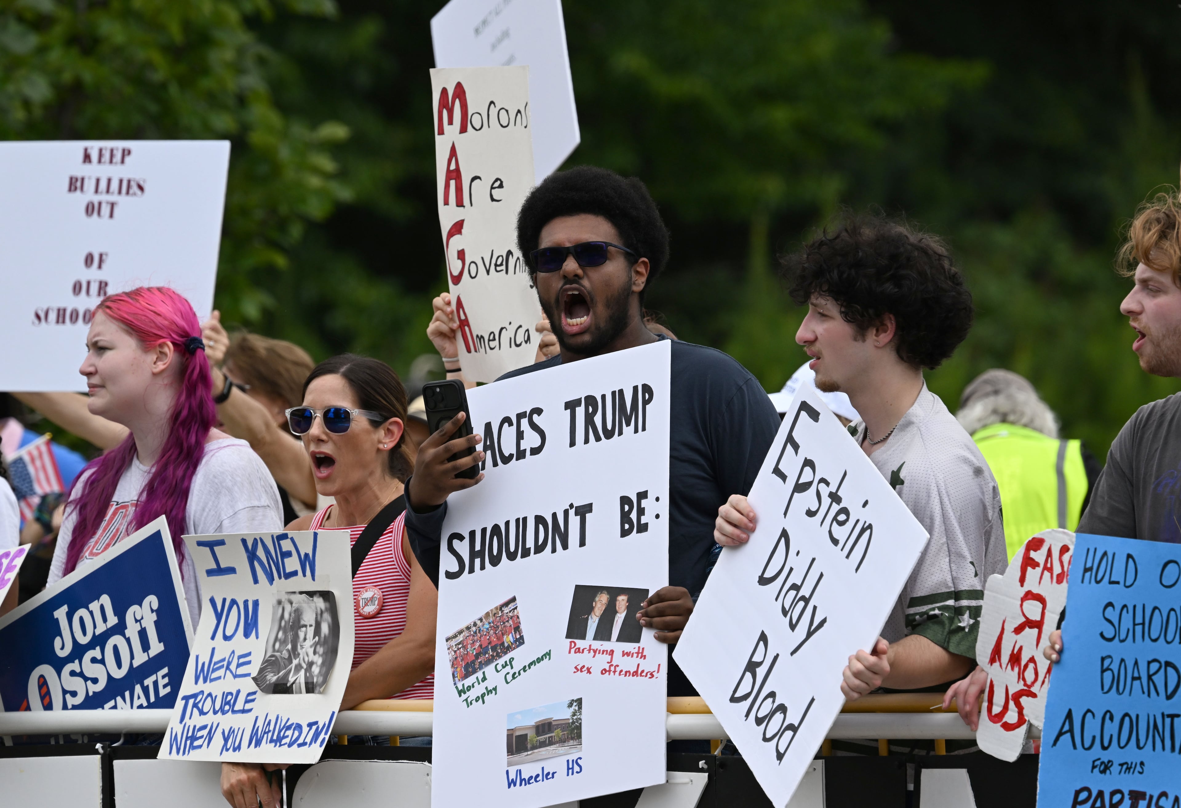 Protesters opposed to President Donald Trump's visit hold signs and line a street as he arrives outside Wheeler High School on Wednesday, July 22, 2026, in Marietta. President Donald Trump is visiting Cobb County’s Wheeler High School on Wednesday to promote a new investment account for children. (Hyosub Shin/AJC)