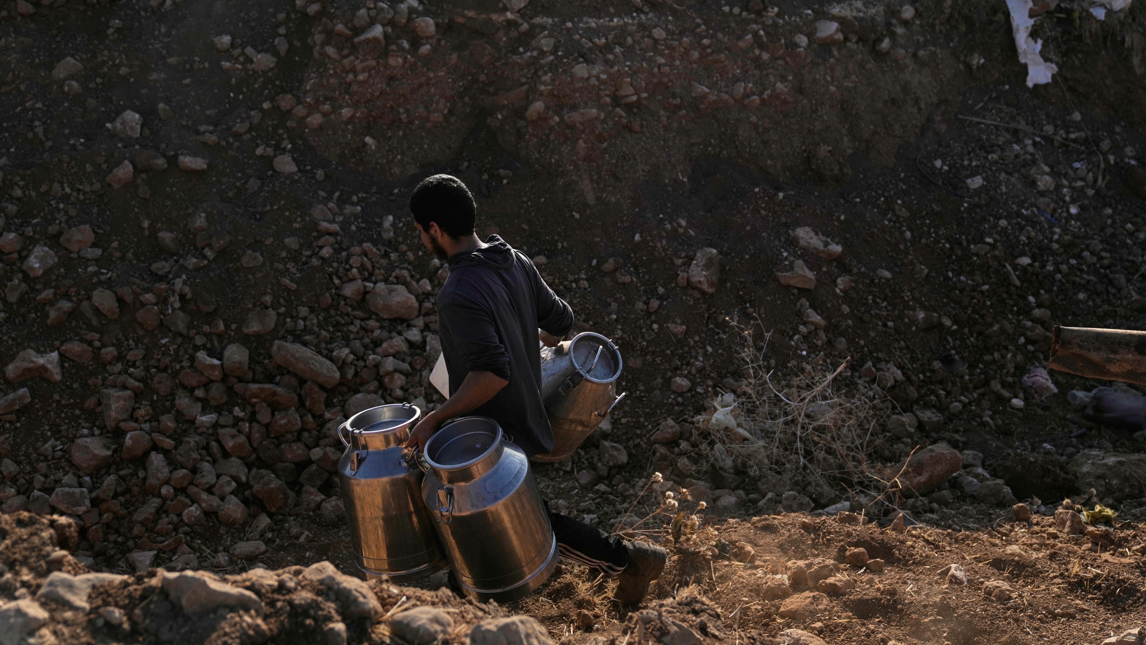 A Palestinian farmer carries containers of milk from their livestock across a trench dug by the Israeli army in a road leading to the West Bank hamlet of Khirbet Ras al-Ahmar, southeast of Tubas, on their way to sell it Saturday, Sept. 19, 2026. (AP Photo/Majdi Mohammed)