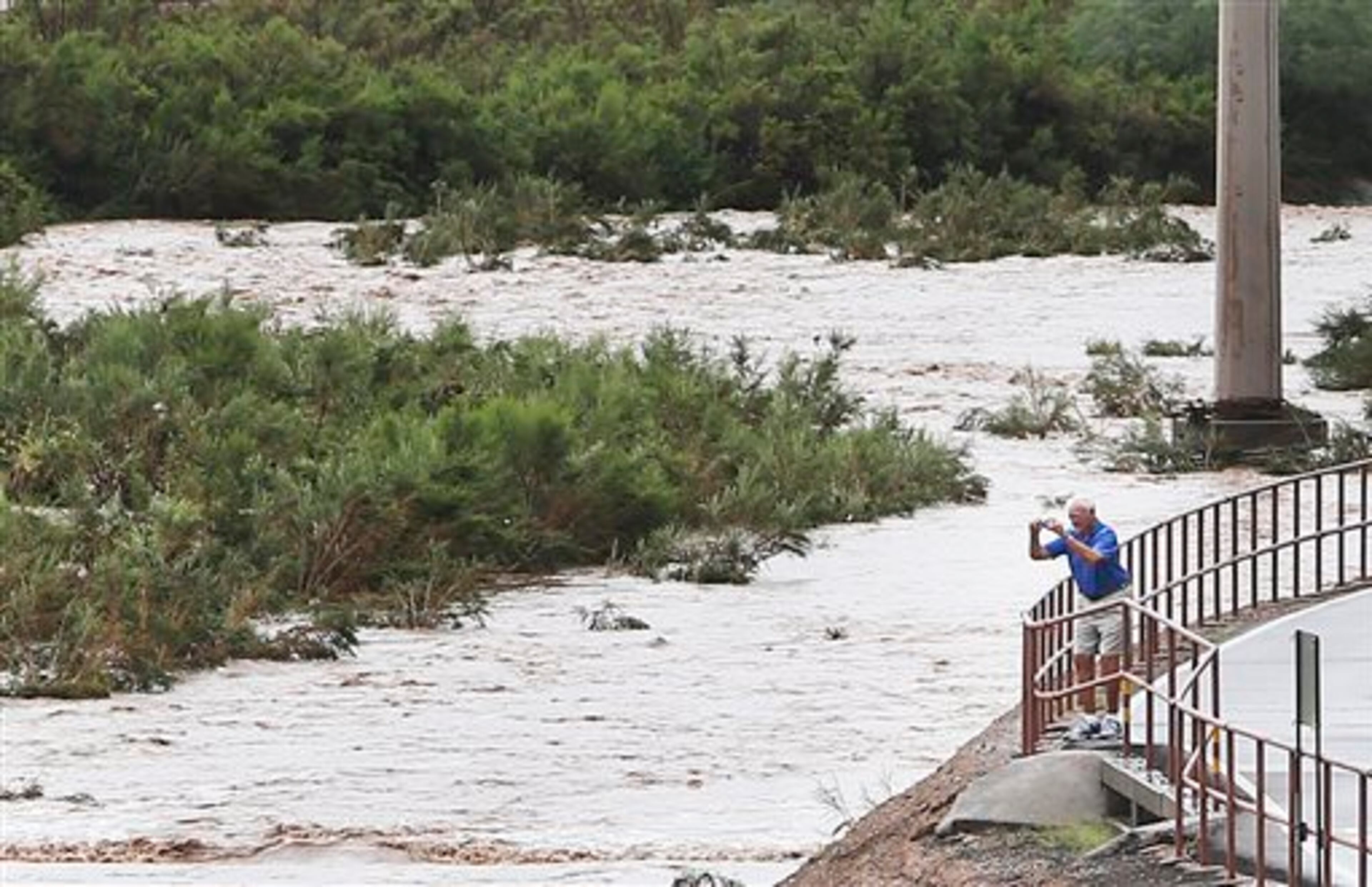 A man takes a picture of the torrents of monsoon storm runoff in the Rillito River near North Craycroft Road south of East River Road on Monday, Sept. 8, 2014, in Tucson, Ariz. (AP Photo/Arizona Daily Star, Mike Christy)