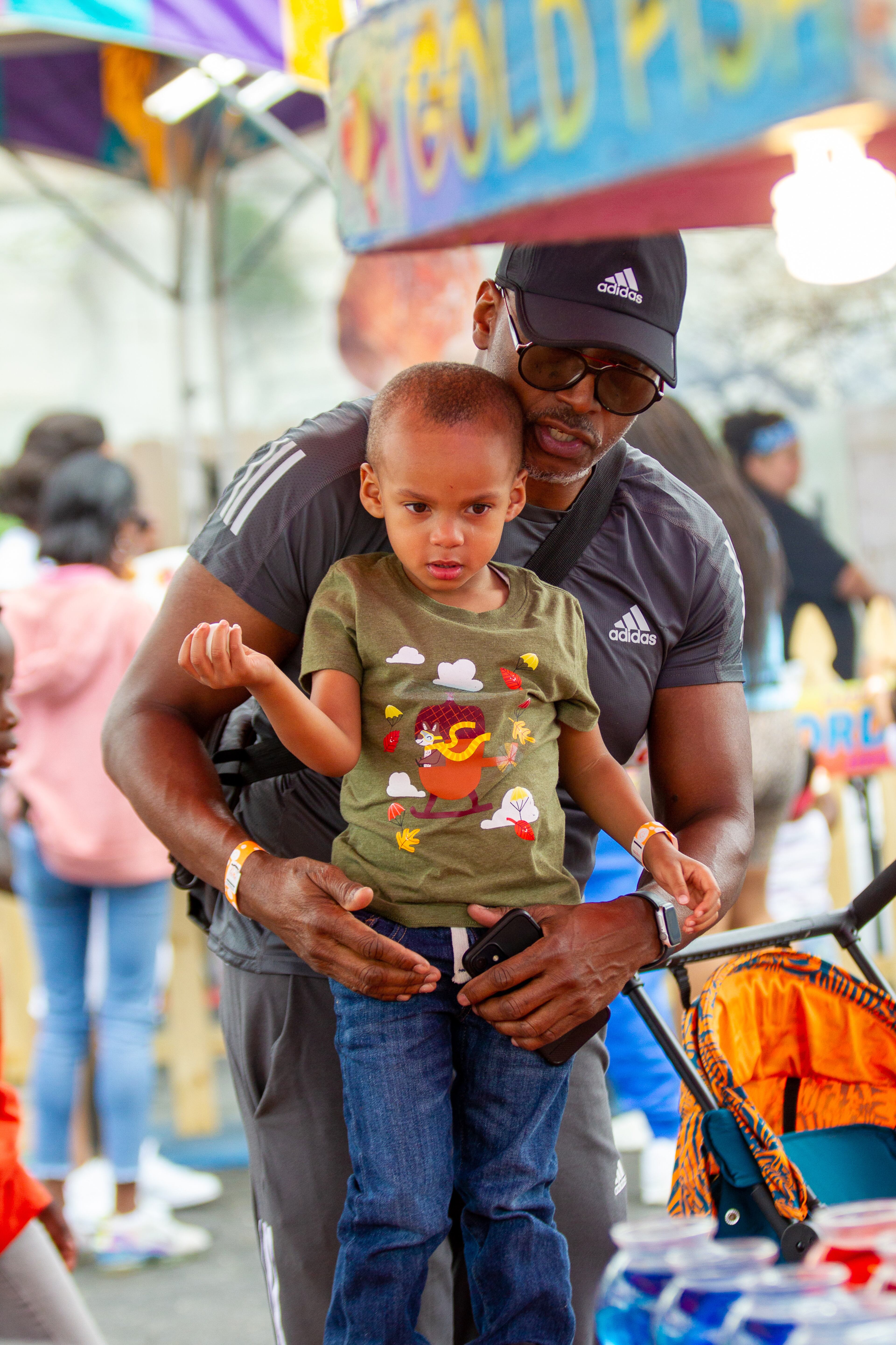 Kenny Riles helps his grandson Kayin, 3, try to win a goldfish by throwing a ping-pong ball into a bowl at the Atlanta Fair on Sunday, March 6, 2022. (Photo by Steve Schaefer for The Atlanta Journal-Constitution)