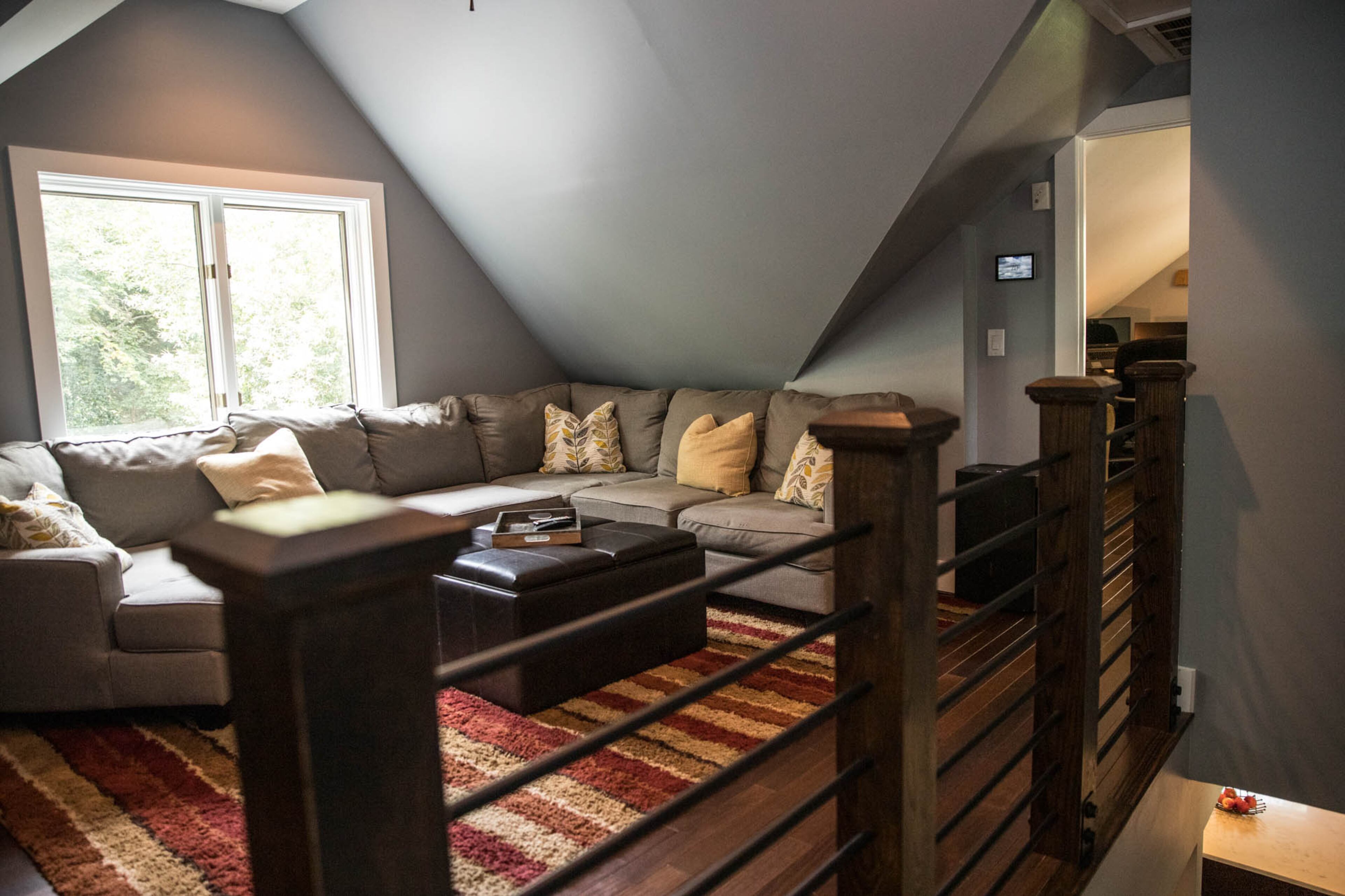 The family room at the top of the stairs is homeowners Adam Perry and Ben Ratossa's favorite room of their newly renovated upstairs. A large sectional from Ashley HomeStore now fits comfortably beneath the newly raised ceilings, creating a perfect place for the couple to lounge, and wood and metal railings, one of Perry's favorite new features, section off the space from the stairs below.