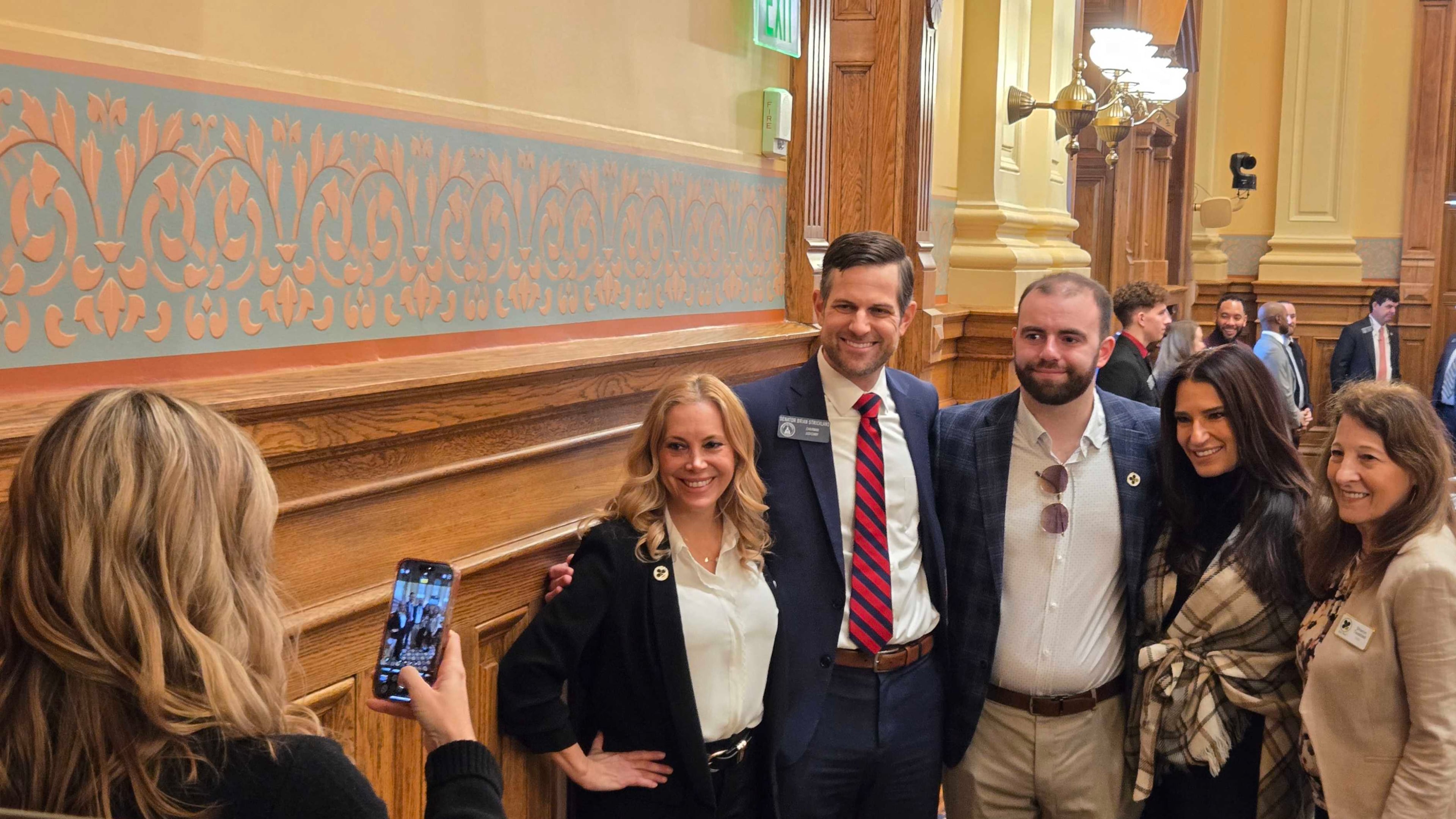 "Love on the Spectrum" star Connor Tomlinson (center) is urging Georgia lawmakers to pass a bill creating an autism specialty license plate and requiring first responders to be trained in autism response. From left: Layla Luna (autism advocate and founder of Just Bee), Sen. Brian Strickland, Connor Tomlinson, Lise Smith (Connor's mother) and Sharon Twaddell (COO of Just Bee). Taking the photo is Strickland's wife Lindsay. (Maya Prabhu/AJC)