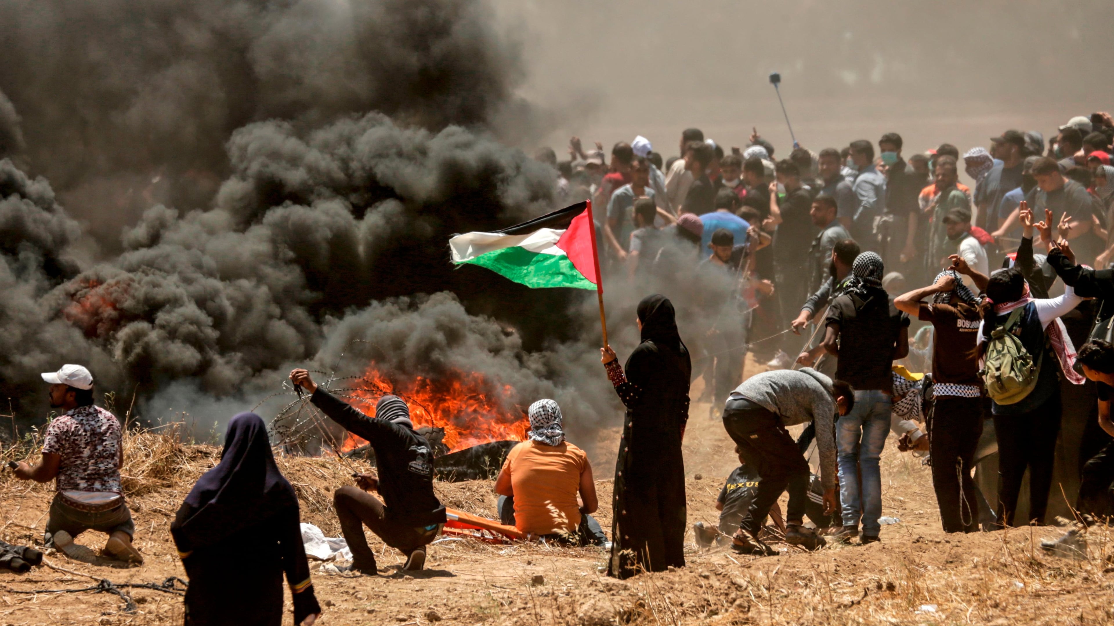 A Palestinian woman holding her national flag looks at clashes with Israeli forces near the border between the Gaza strip and Israel east of Gaza City on May 14, 2018, as Palestinians protest over the inauguration of the U.S. embassy following its controversial move to Jerusalem.