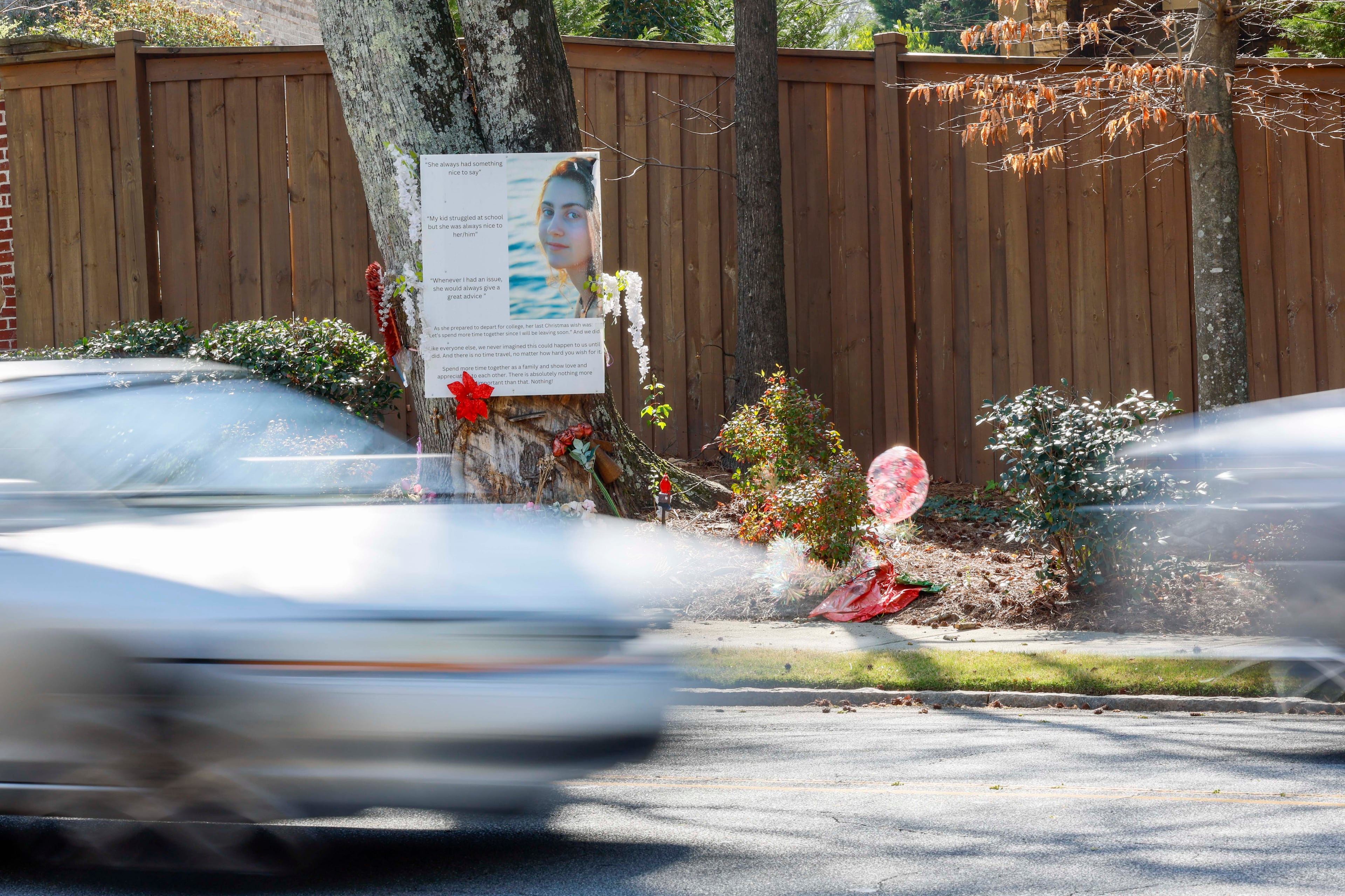 Cars on Oak Grove Road drive past a memorial for Sophia Lekiachvili at the site of the crash that killed her in February 2024. She was a senior at Lakeside High School in DeKalb County. On the poster are the words, “Let’s spend more time together since I will be leaving soon.” (Miguel Martinez/AJC)