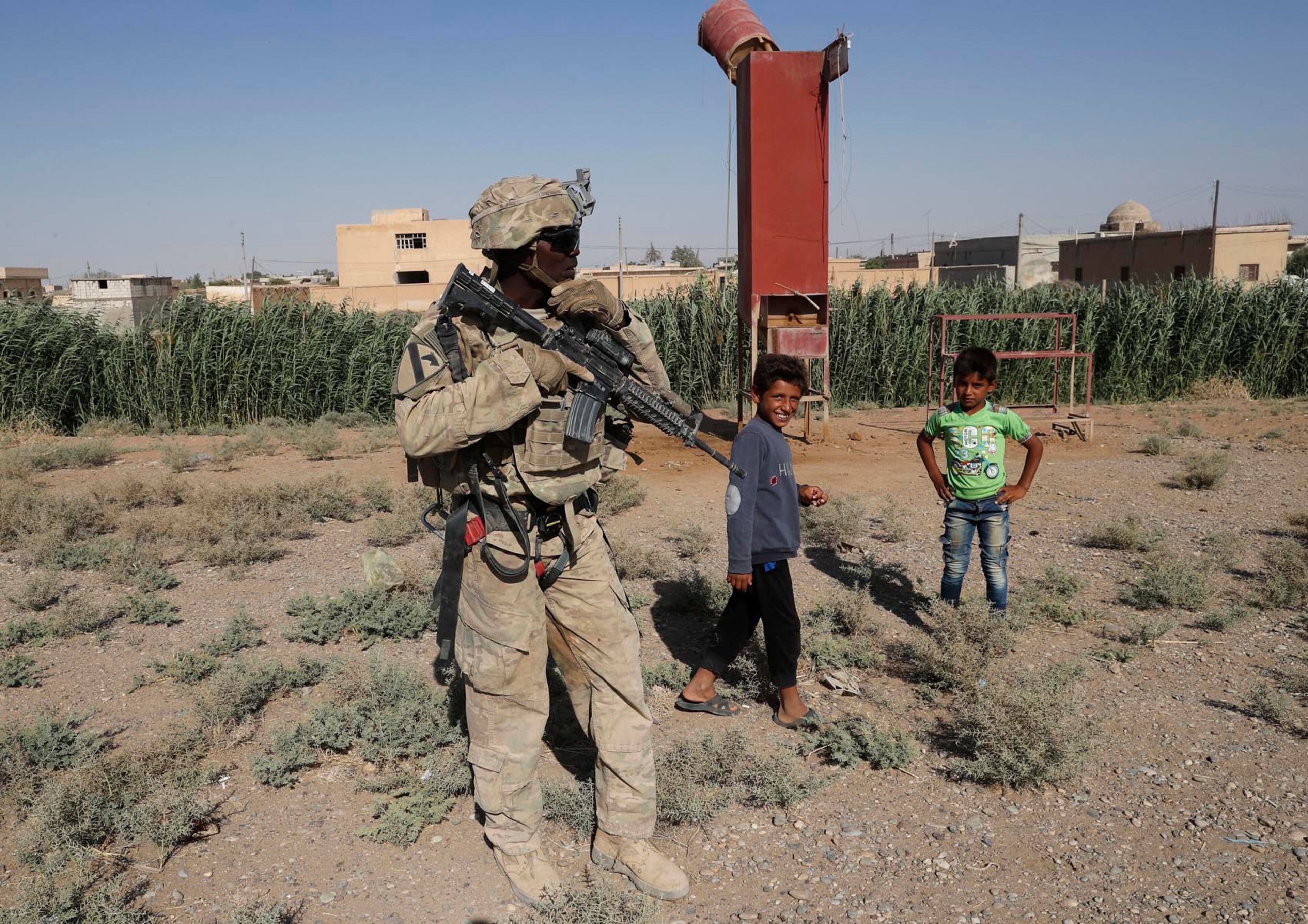 A U.S. soldier stands near Syrian children on a road that links to Raqqa, Syria, Wednesday, July 26, 2017. The U.S. has up to 1,000 troops in Syria mostly involved in training and advising the local forces against IS. Kurdish forces have gained confidence in light of open U.S. support to their forces, particularly as the battle for Raqqa took off. (AP Photo/Hussein Malla)