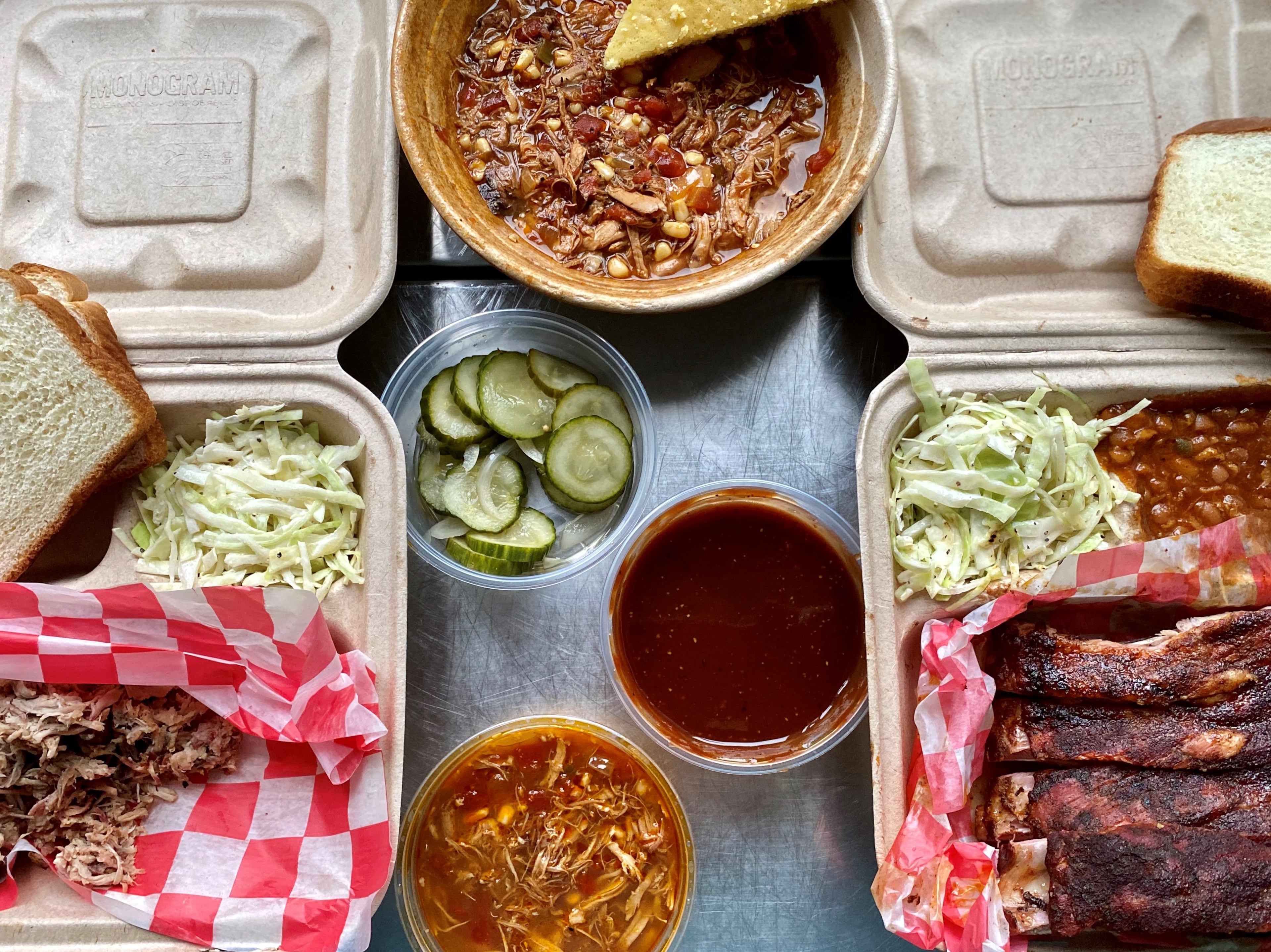 A takeout feast from BBQ Cafe in Decatur: Pulled pork with slaw and Brunswick stew; a meal-size bowl of stew with cornbread; and ribs with slaw and baked beans. In the middle are house-made bread and butters and the house sauce.
Wendell Brock for The Atlanta Journal-Constitution
