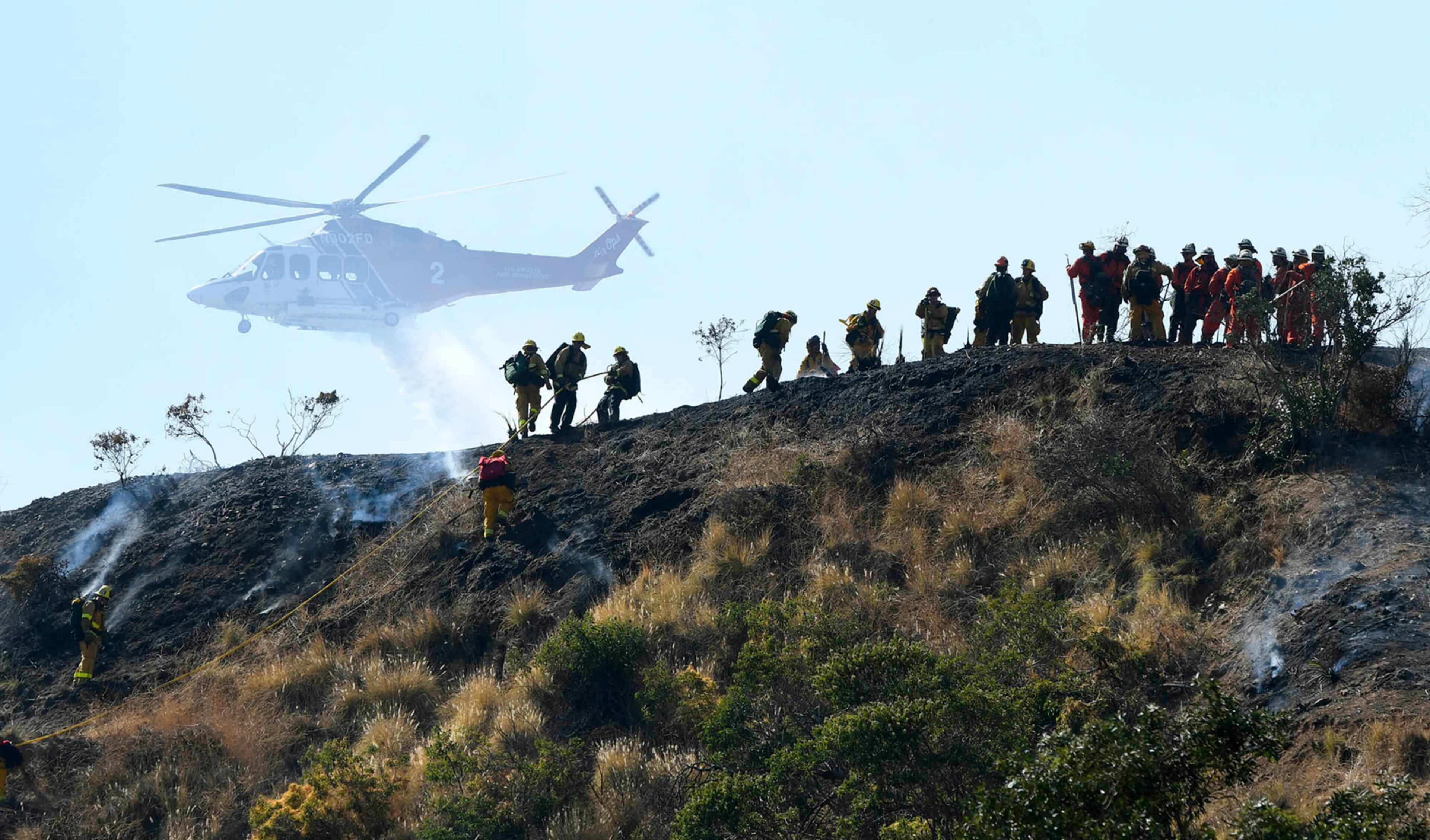 Camp crews pull a line up a hill while a slow moving grass and brush fire threatens homes in Burbank, Calif., Wednesday, June 28, 2017. Dozens of homes were under mandatory evacuation orders on the suburban edges of Burbank, where flames raced uphill through tinder-dry grass. (John McCoy/Los Angeles Daily News via AP)