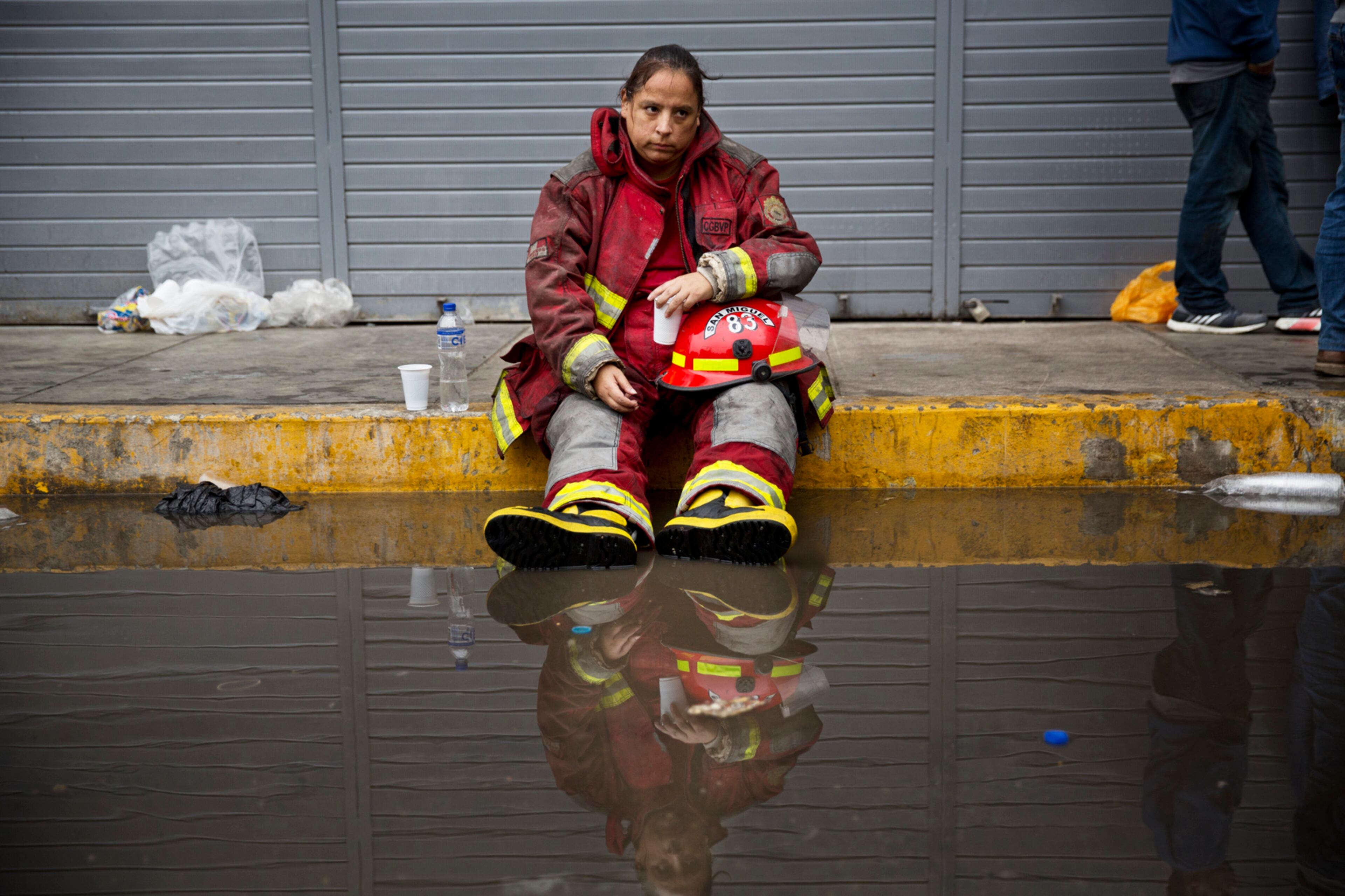 Exhausted firefighter Julia Alegre Smith rests after working to battle a warehouse fire in Lima, Peru, Friday, June 23, 2017. The fire has been raging for nearly a day in Peru's capital where tons of flammable materials were stored. At least 4 people are reported disappeared inside the warehouse according to authorities. (AP Photo/Rodrigo Abd)