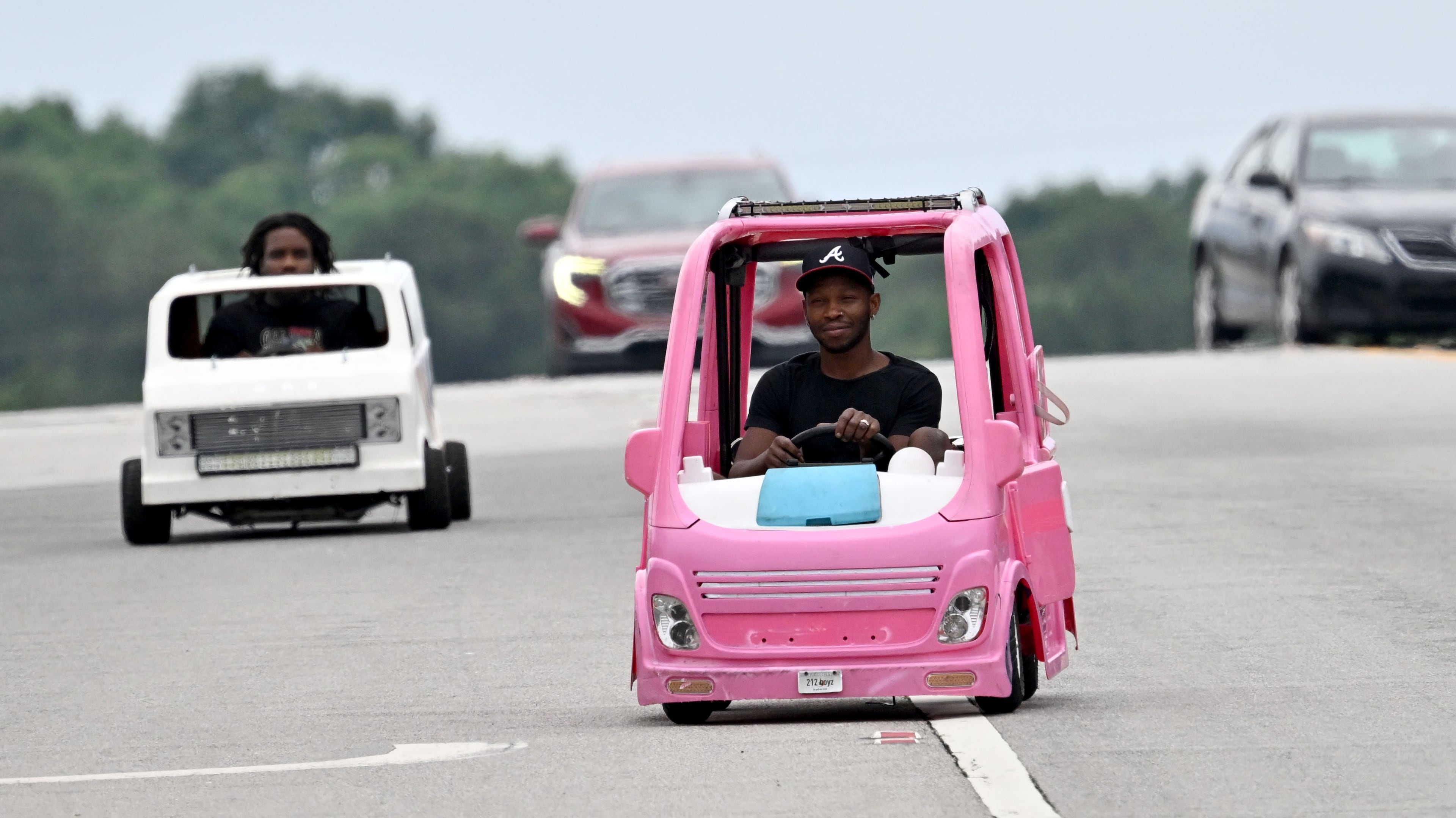Mali “Sota” Hightower drives his modified, gas-powered Barbie Dream camper as his friend Marvelous Gainey follows close behind in his modified minicar on Tuesday, June 9, 2026, in Ellenwood. Hightower decided to put his interest in modified kids' cars to use when gas prices began to rise, driving the pink vehicle to his day job as a contractor. (Hyosub Shin/AJC)