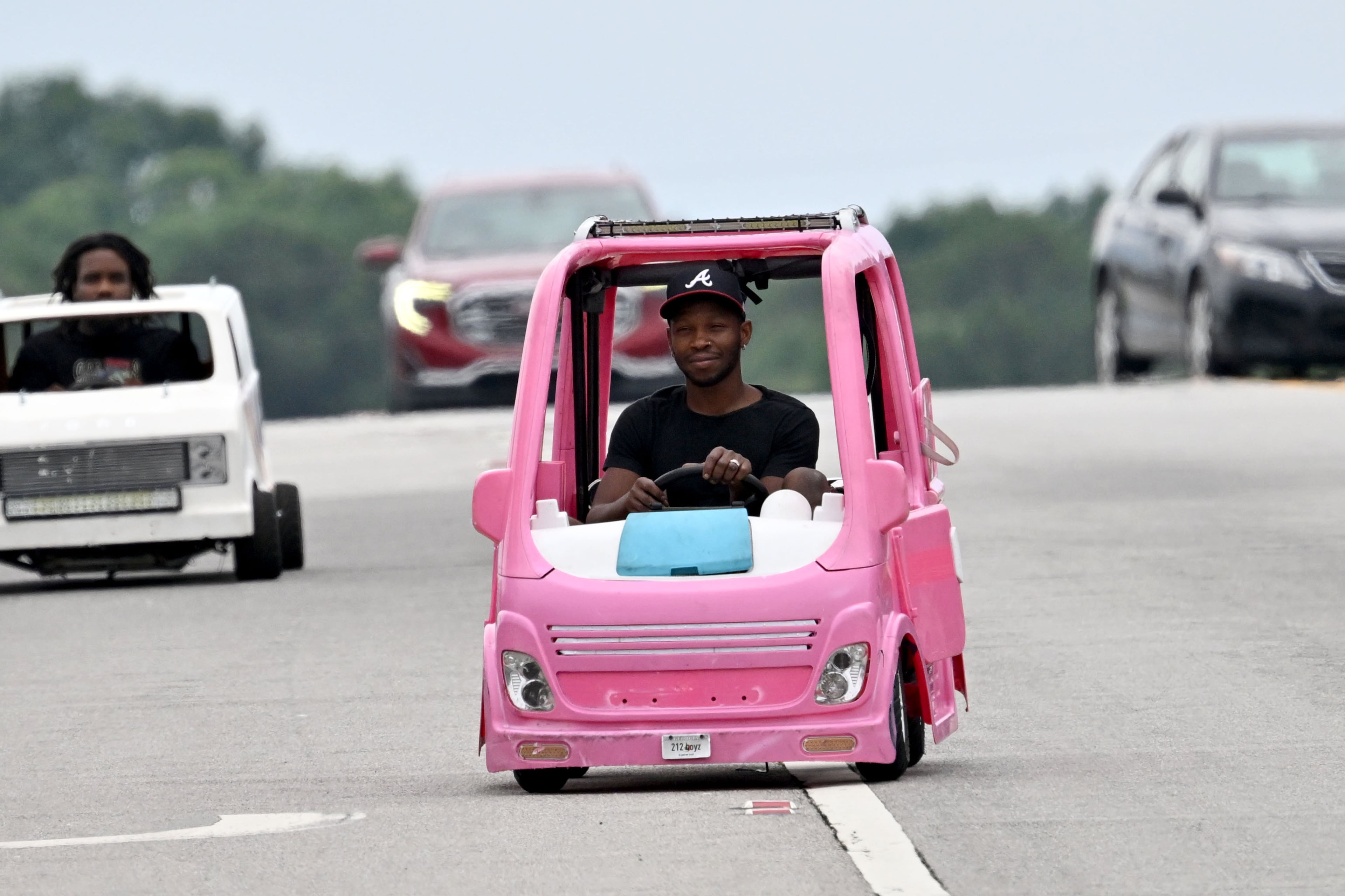 Mali “Sota” Hightower drives his modified, gas-powered Barbie Dream camper as his friend Marvelous Gainey follows close behind in his modified minicar on Tuesday, June 9, 2026, in Ellenwood. Hightower decided to put his interest in modified kids' cars to use when gas prices began to rise, driving the pink vehicle to his day job as a contractor. (Hyosub Shin/AJC)