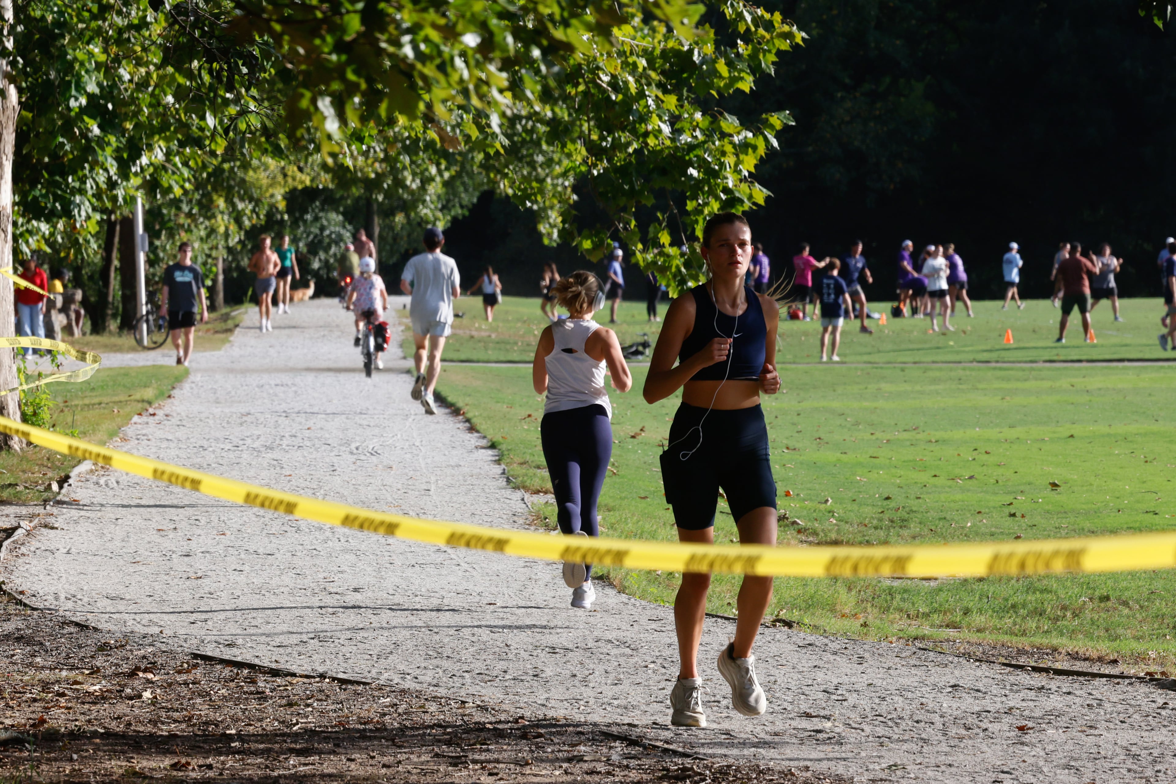 A runner jogs past crime scene tape in Piedmont Park on Wednesday, Sept. 9, 2026, in Atlanta. One man has been charged in the gunfire incident, police say. (Arvin Temkar/AJC)